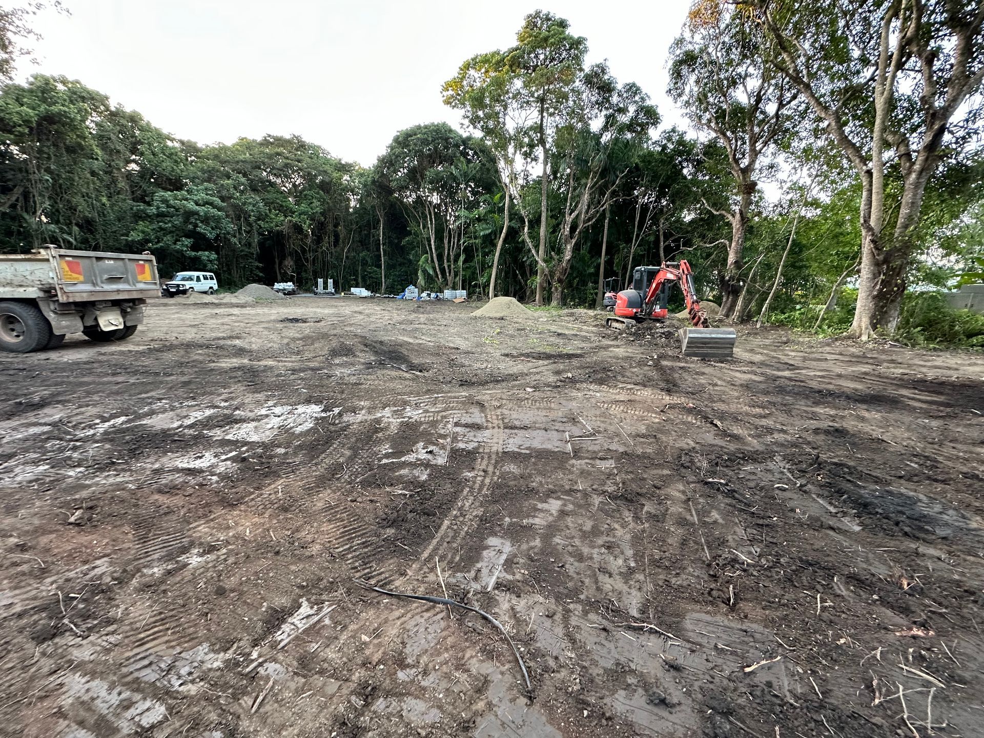 landscape preparing in dirt field with red bobcat with trees in the back — Cairns Earthmoving Solutions In Holloways Beach, QLD