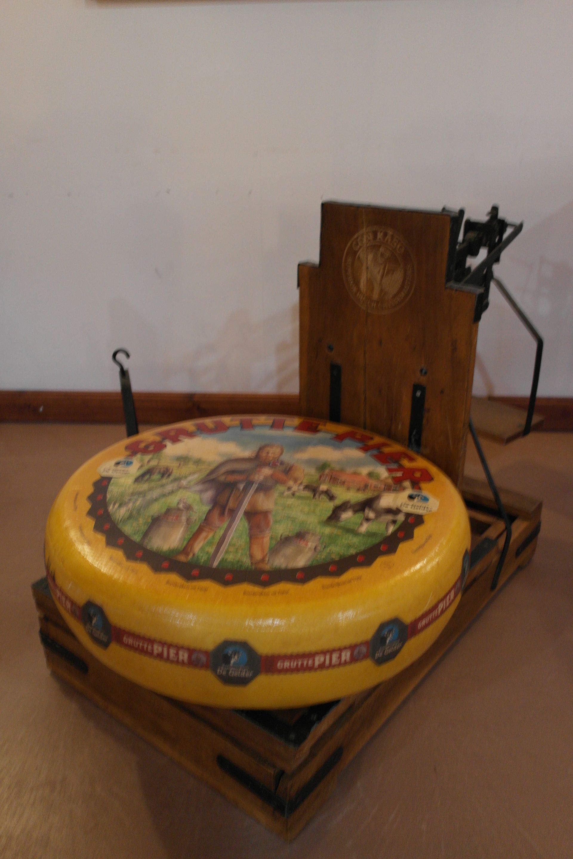 Ein großer gelber Käselaib mit einem kleineren abgeschnittenen Stück auf einem Holzbrett.