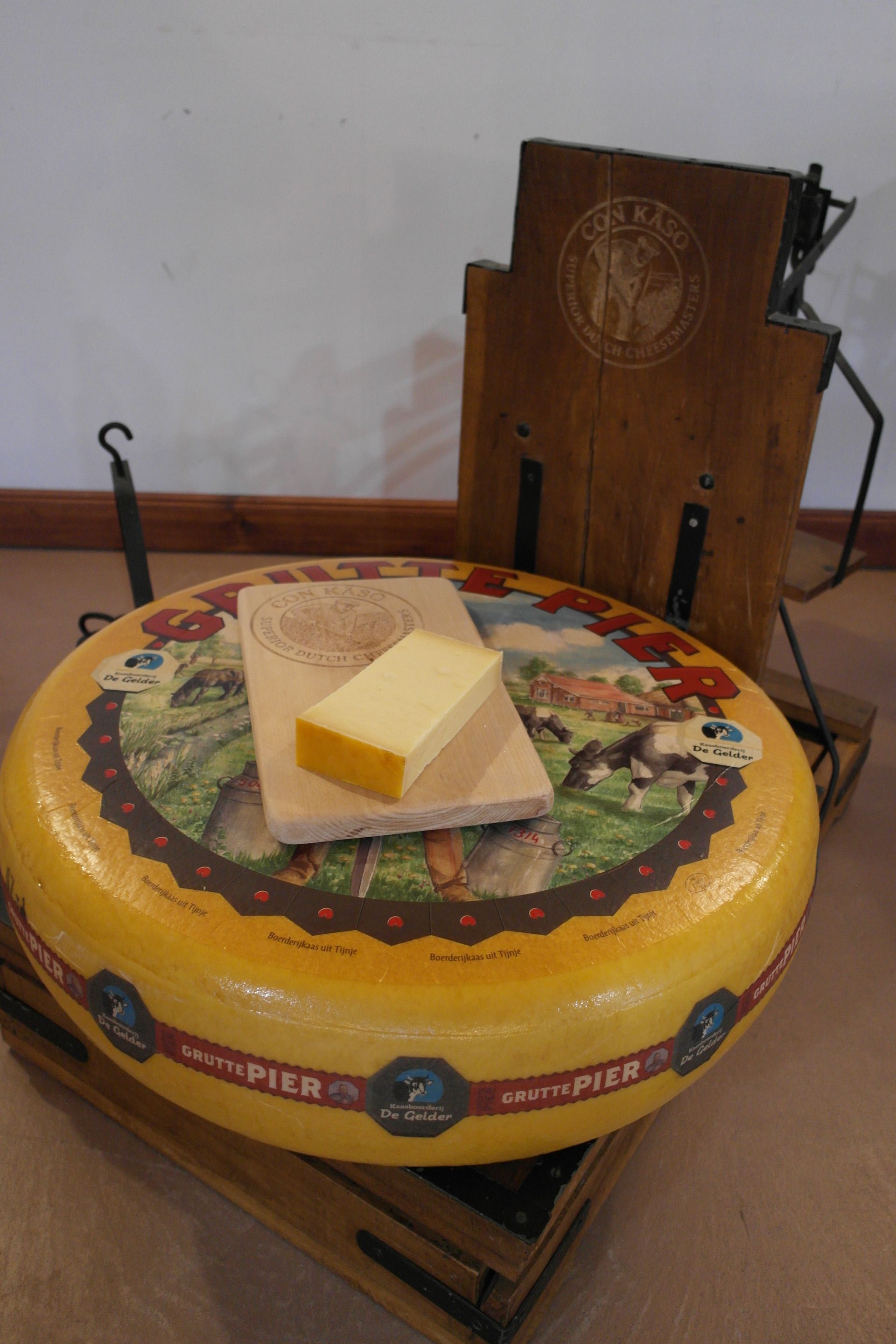 Ein großer gelber Käselaib mit einem kleineren abgeschnittenen Stück auf einem Holzbrett.