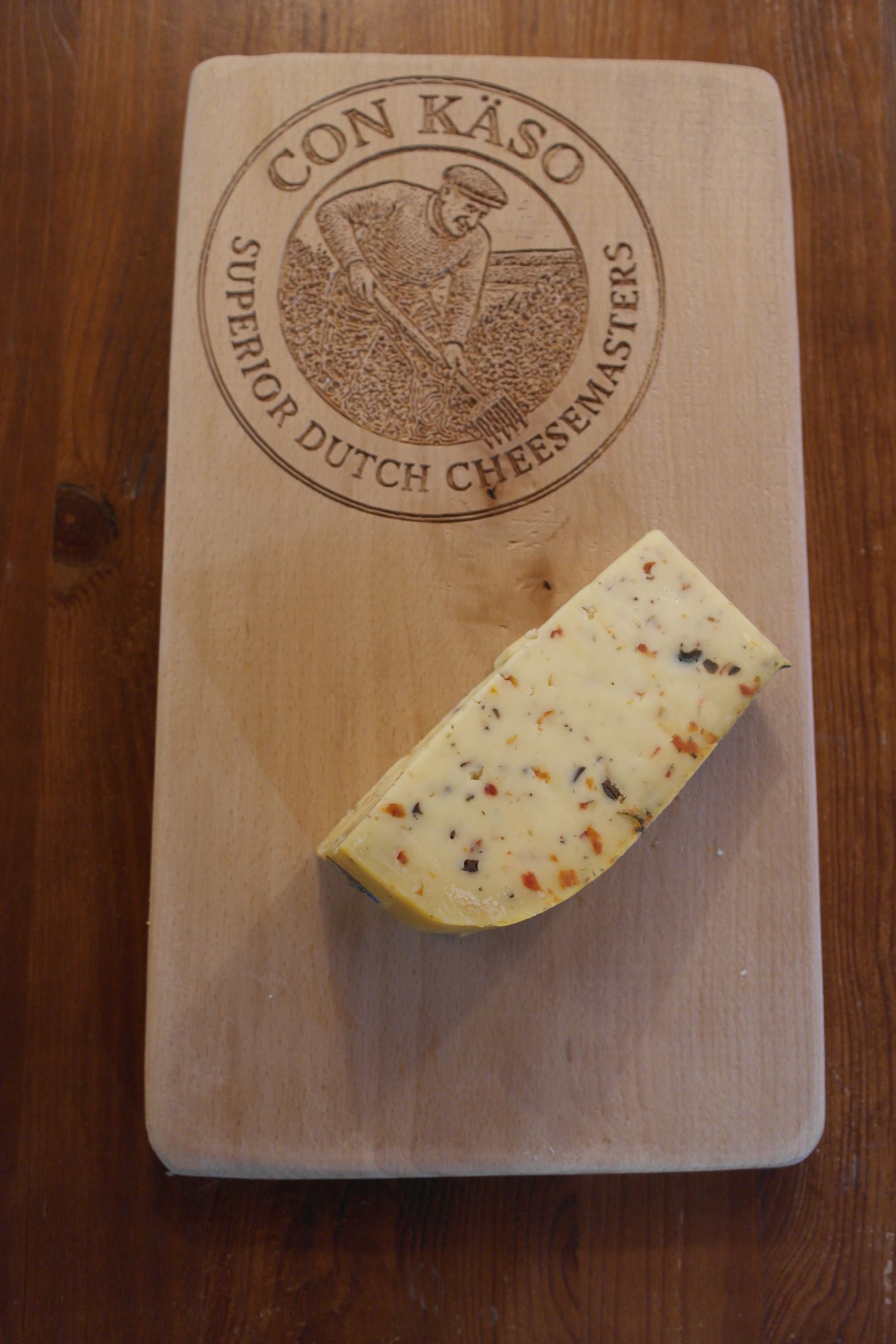 Runder niederländischer De Gelder-Käse mit Kräuterstückchen und einem herausgeschnittenen Stück.