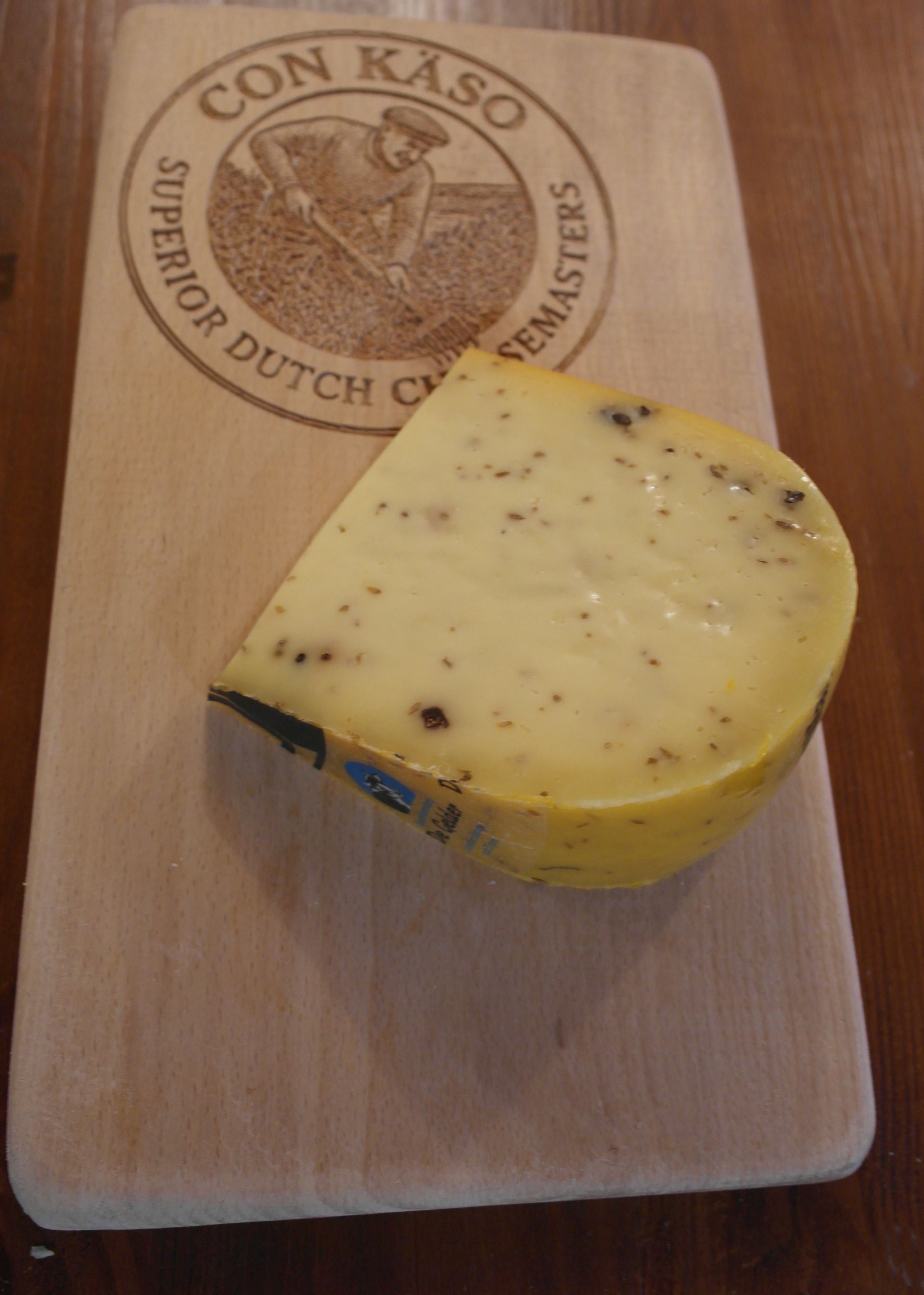 Runder Käselaib von De Gelder mit einem Keil obendrauf; gelb mit dunklen Sprenkeln und Markenzeichen.