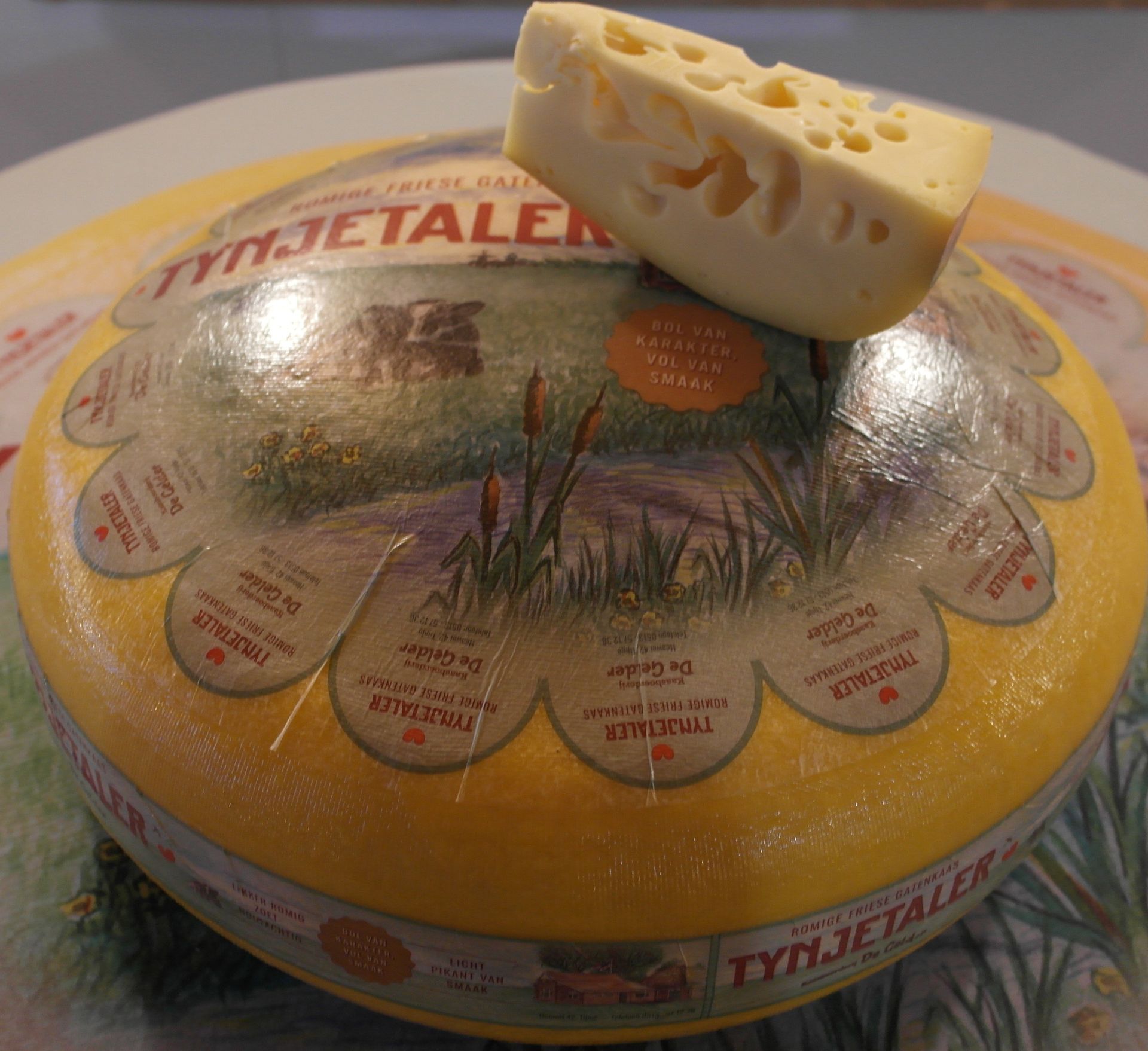 Ein gelber Käselaib mit der Aufschrift „Tynjetaler“ und einem keilförmigen Deckel mit Löchern.