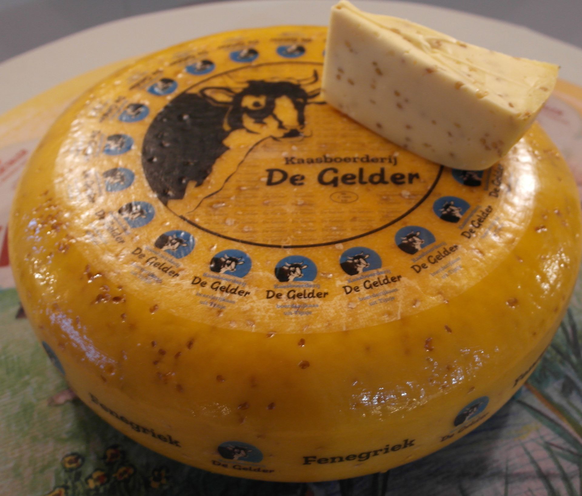 Ein Laib holländischer Käse, „De Gelder“, aus dem ein Stück herausgeschnitten wurde, auf einem weißen Teller.