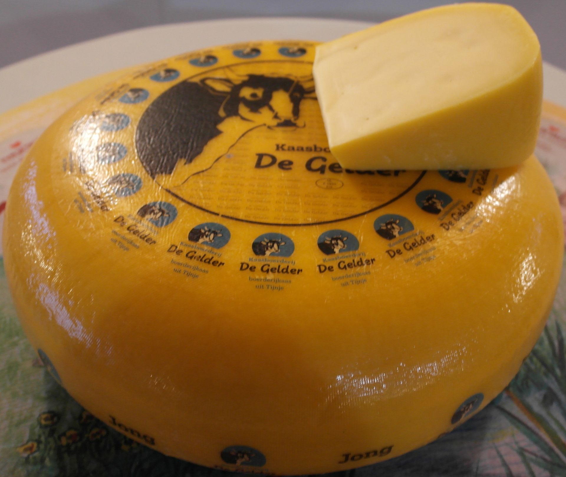 Ein Laib Käse, aus dem ein Stück herausgeschnitten wurde. Gelbe Wachsrinde mit blauen und schwarzen Etiketten.