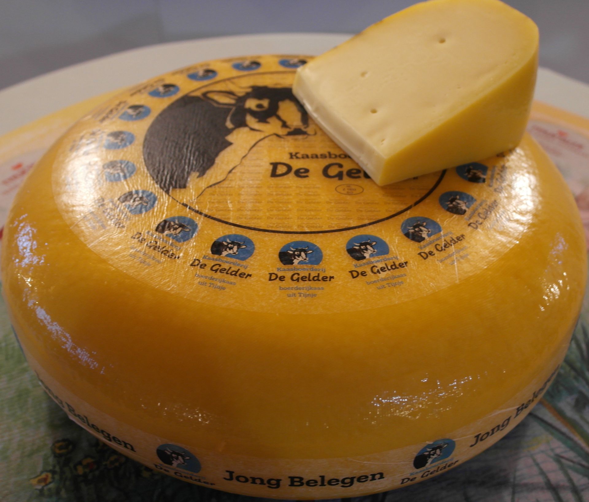 Runder De Gelder Käse mit ausgeschnittenem Keil, goldgelb mit Wachsrinde.
