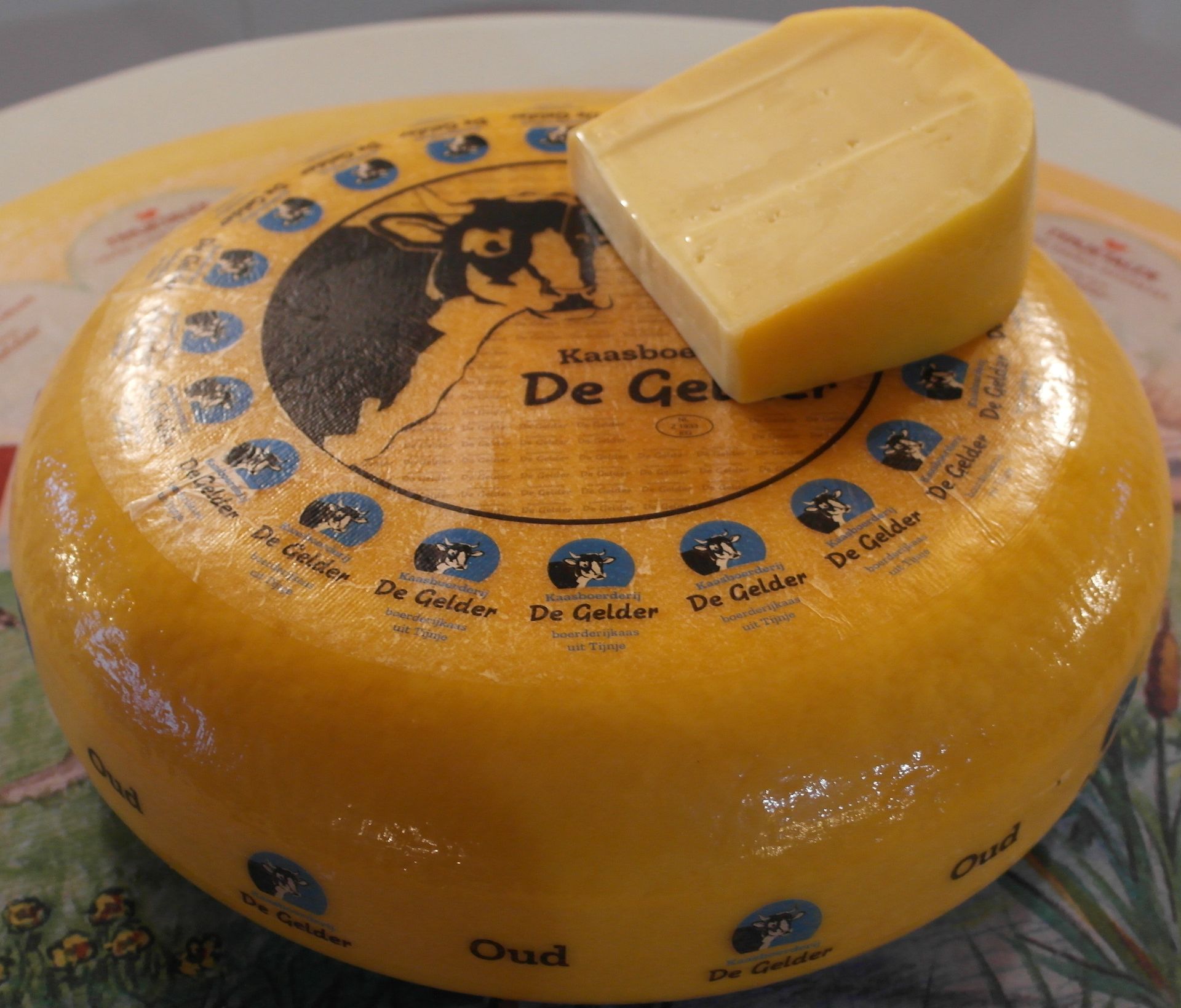 Ein Gouda-Käselaib mit einem abgeschnittenen Stück darauf, auf weißem Untergrund.