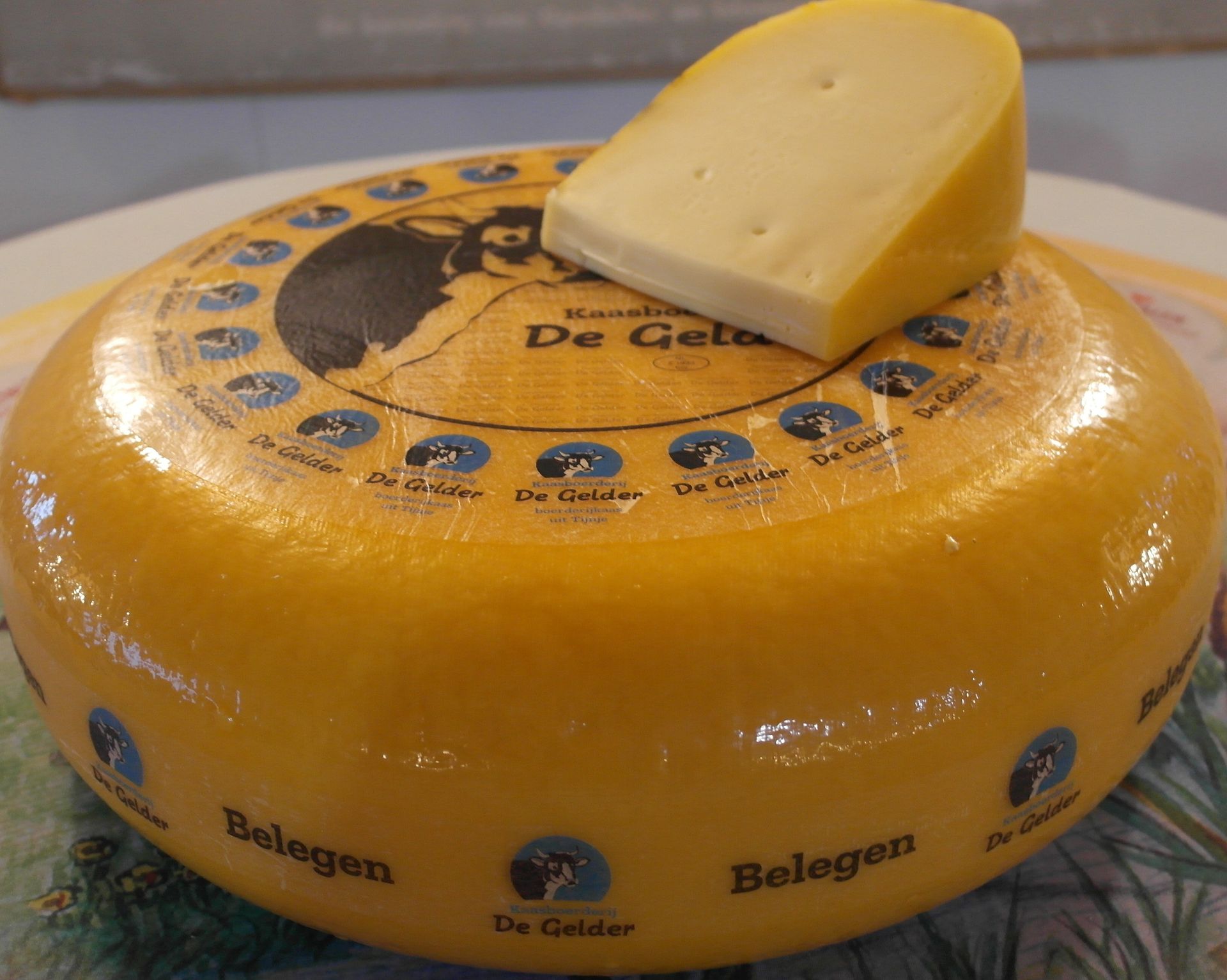 Runder Gouda-Käse mit einem eingeschnittenen Keil obenauf, beschriftet mit „De Gelder“. Gelbe Rinde, helles Inneres.