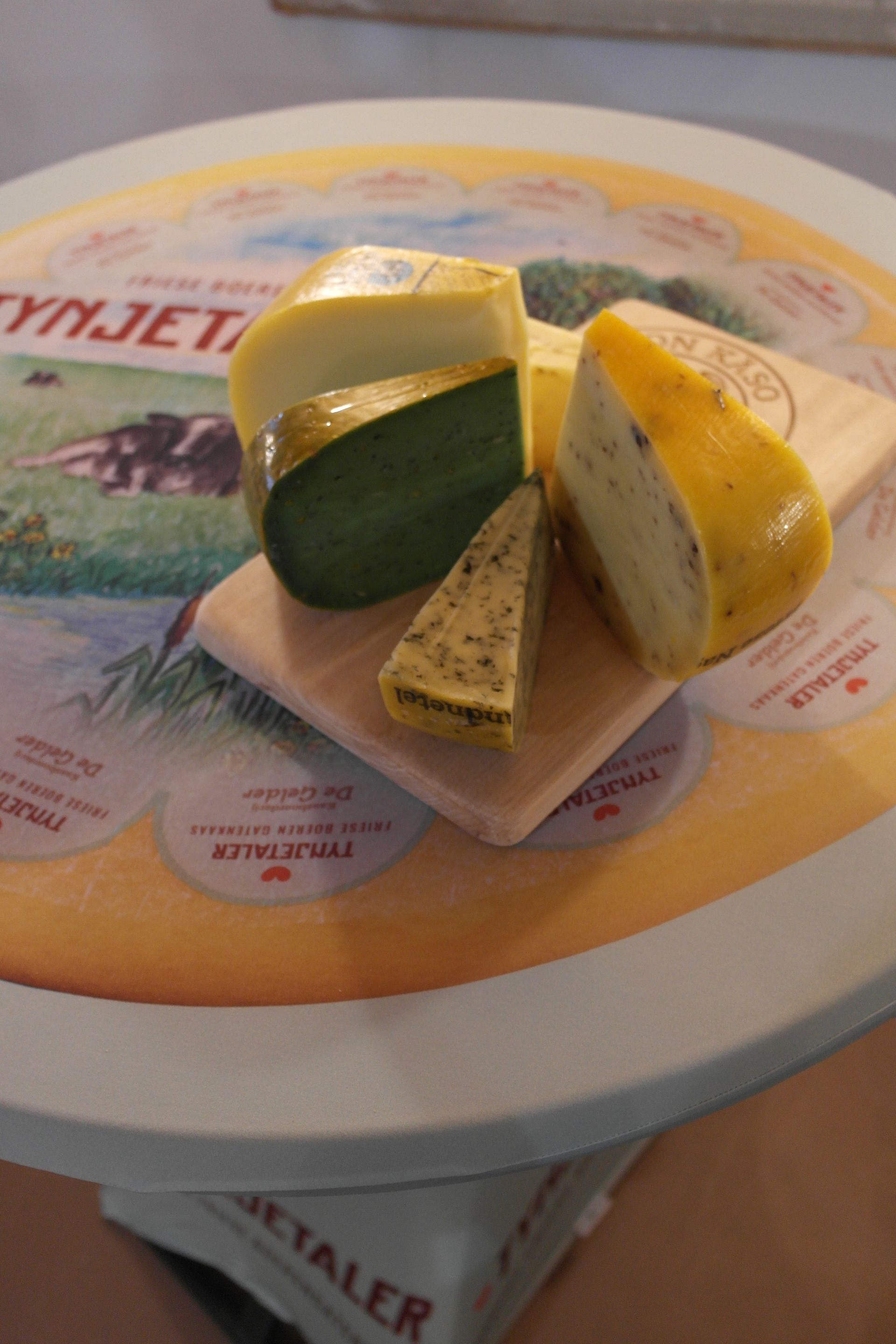 Verschiedene Käsesorten auf einer dekorativen runden Platte. Darunter grüne, gelbe und mit Kräutern überzogene Sorten.