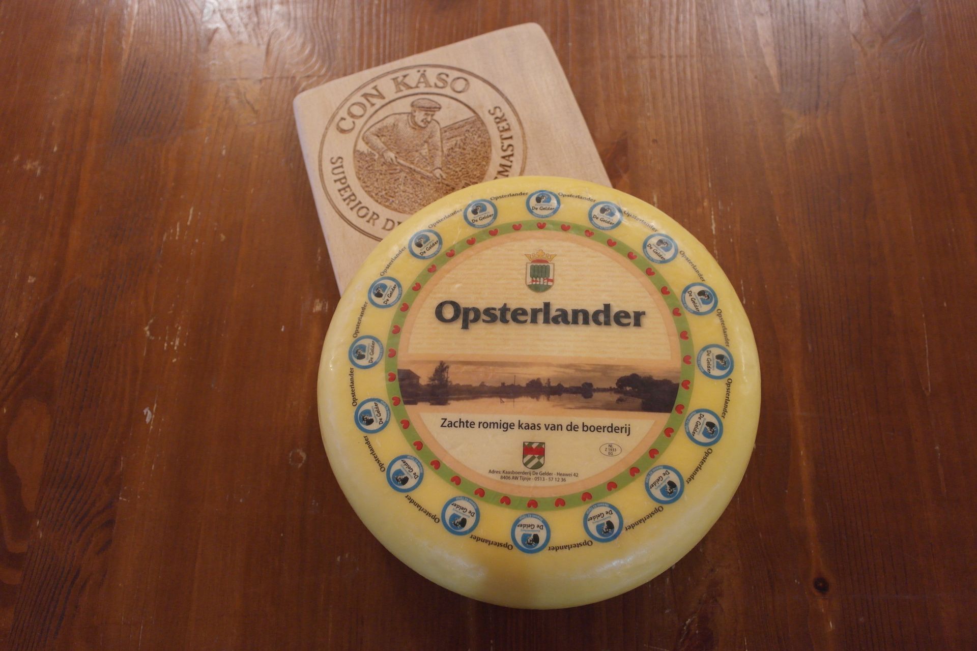 Ein Opsterländer Käselaib auf einem hölzernen Schneidebrett, das auf einem Holztisch steht.