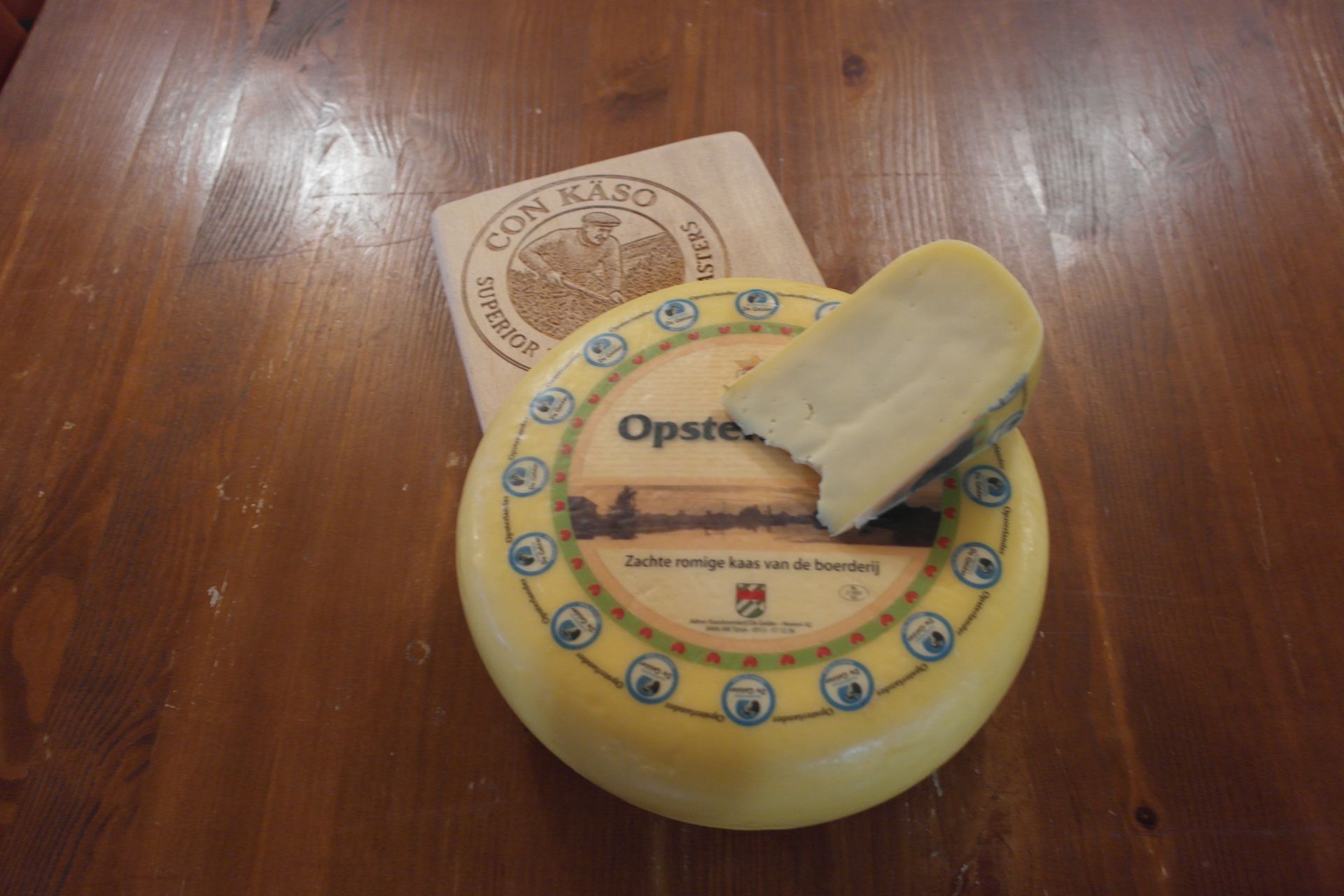 Ein Opsterländer Käselaib auf einem hölzernen Schneidebrett, das auf einem Holztisch steht.