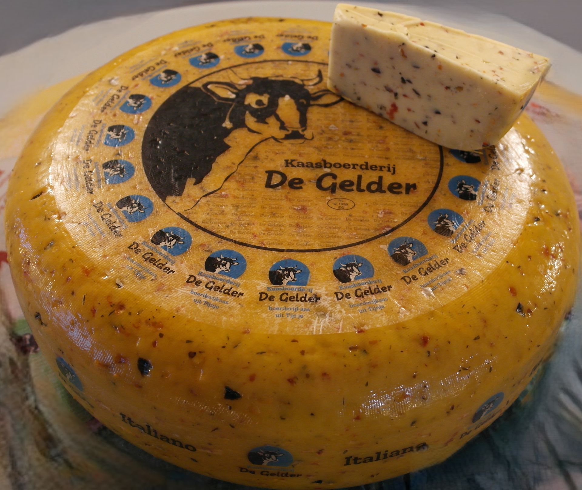 Runder niederländischer De Gelder-Käse mit Kräuterstückchen und einem herausgeschnittenen Stück.