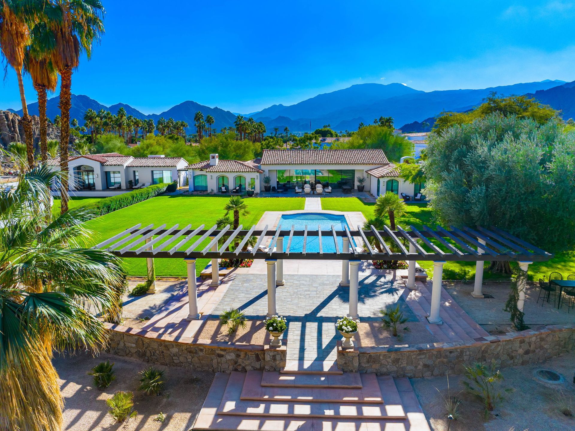 An aerial view of a large house with a pool and mountains in the background.