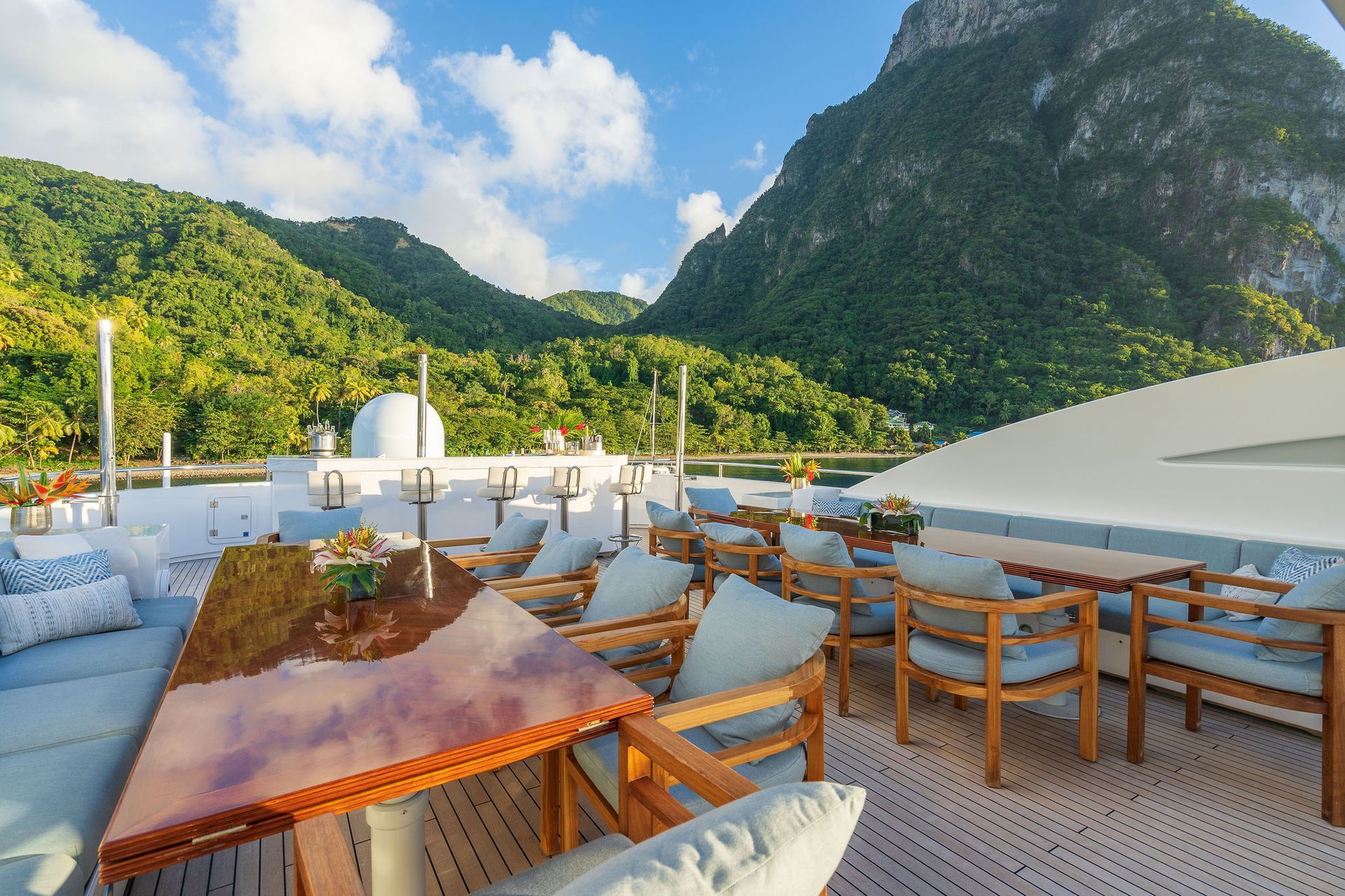 there is a table and chairs on the deck of a yacht with mountains in the background