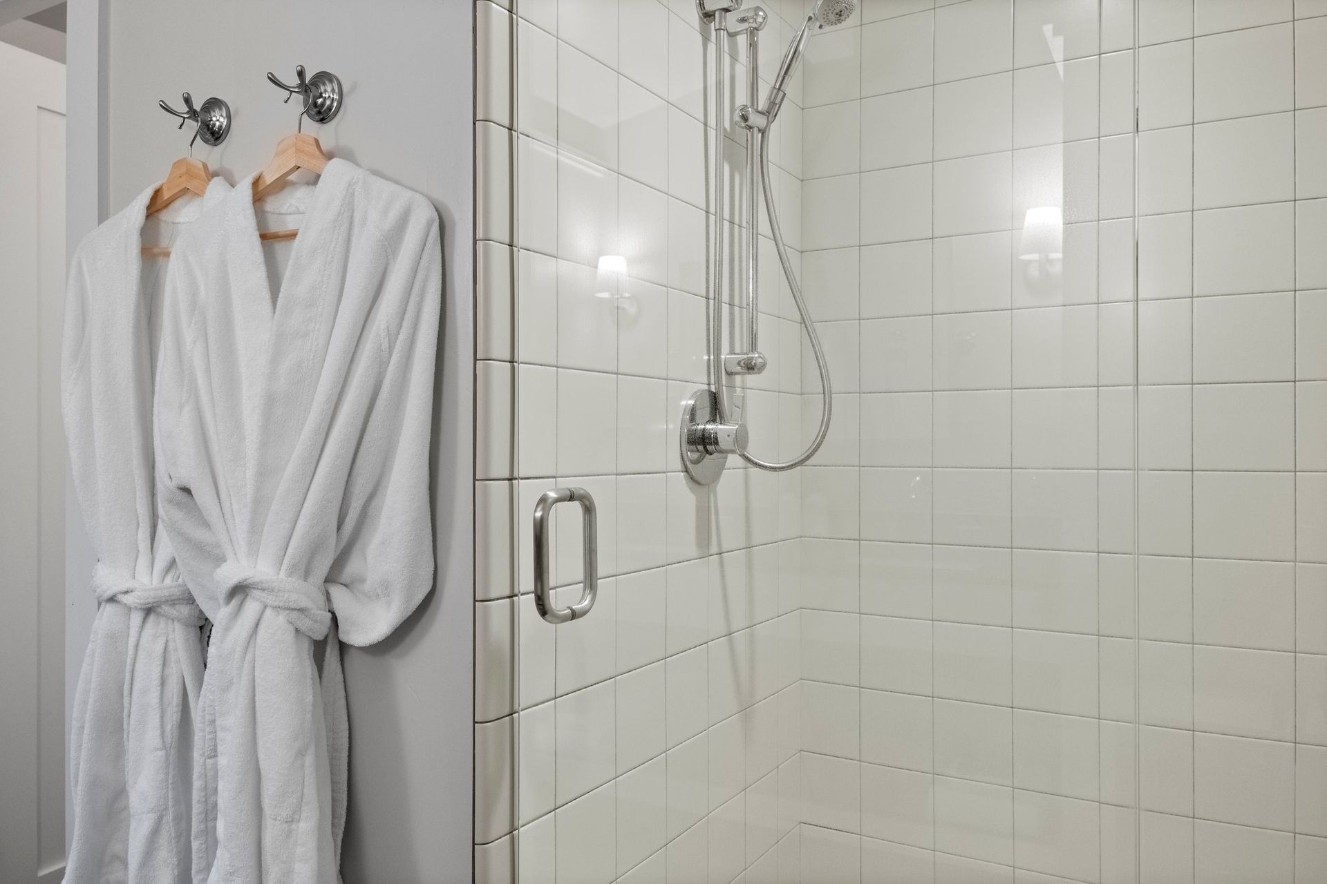 two white robes are hanging in a bathroom next to a shower