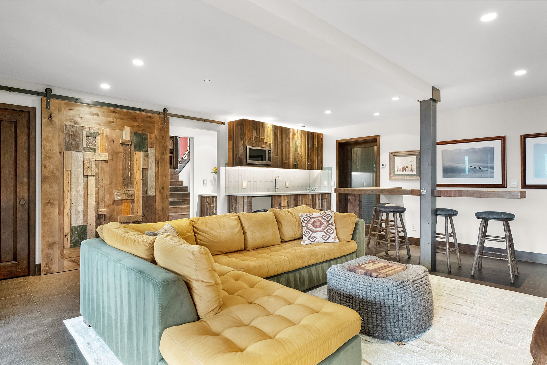 a living room with a yellow sectional couch and a gray ottoman