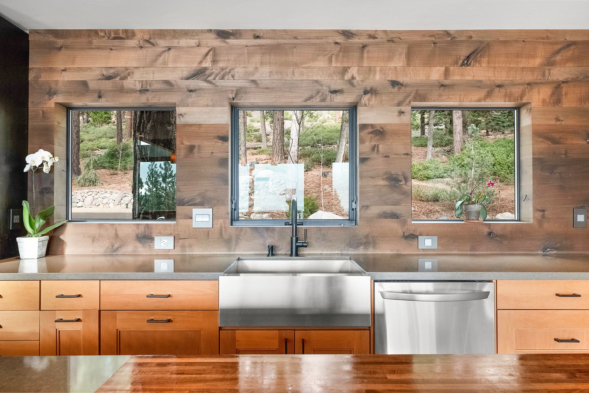 a kitchen with stainless steel appliances, wooden cabinets, a sink, and three windows