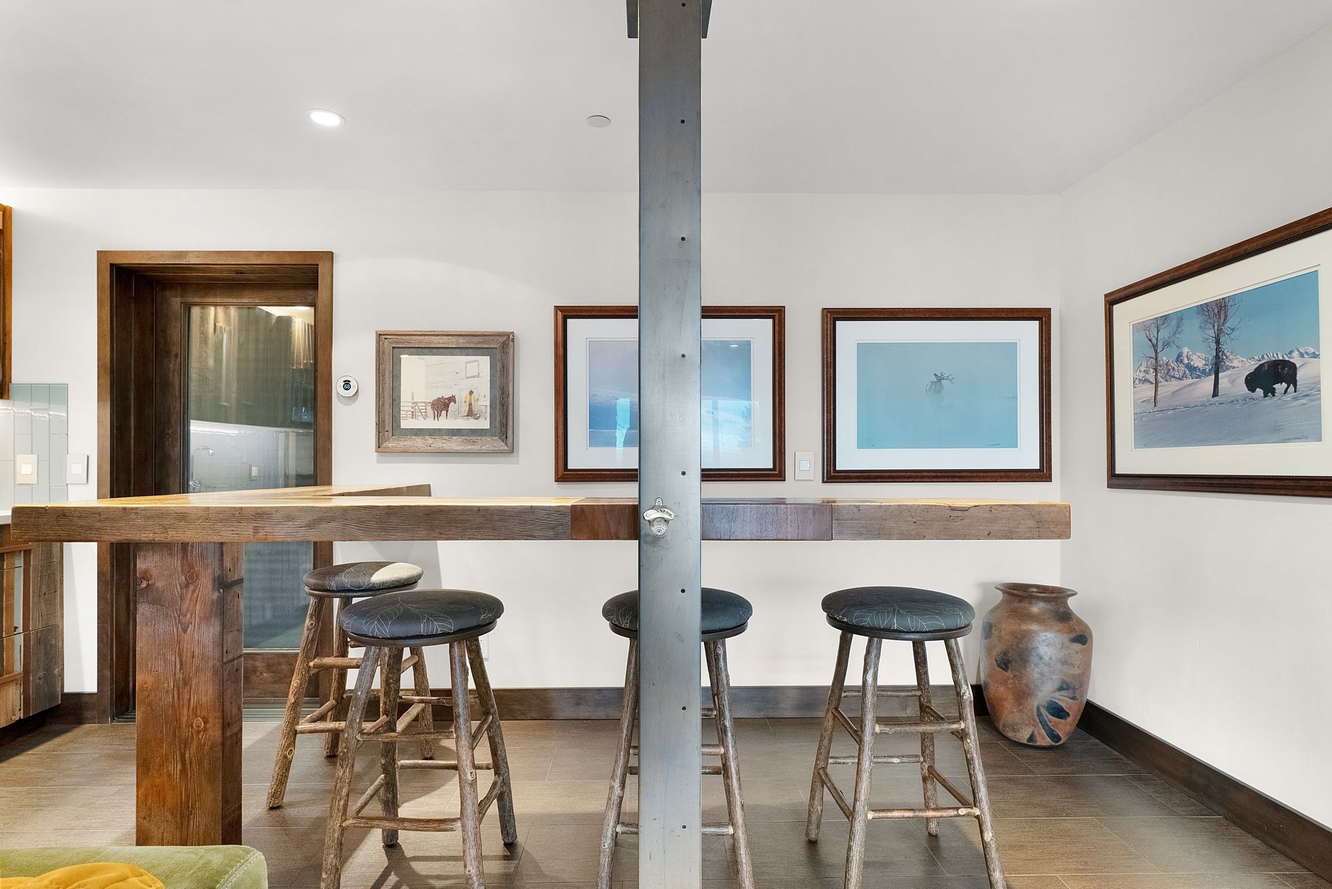 a room with a table and stools and paintings on the wall