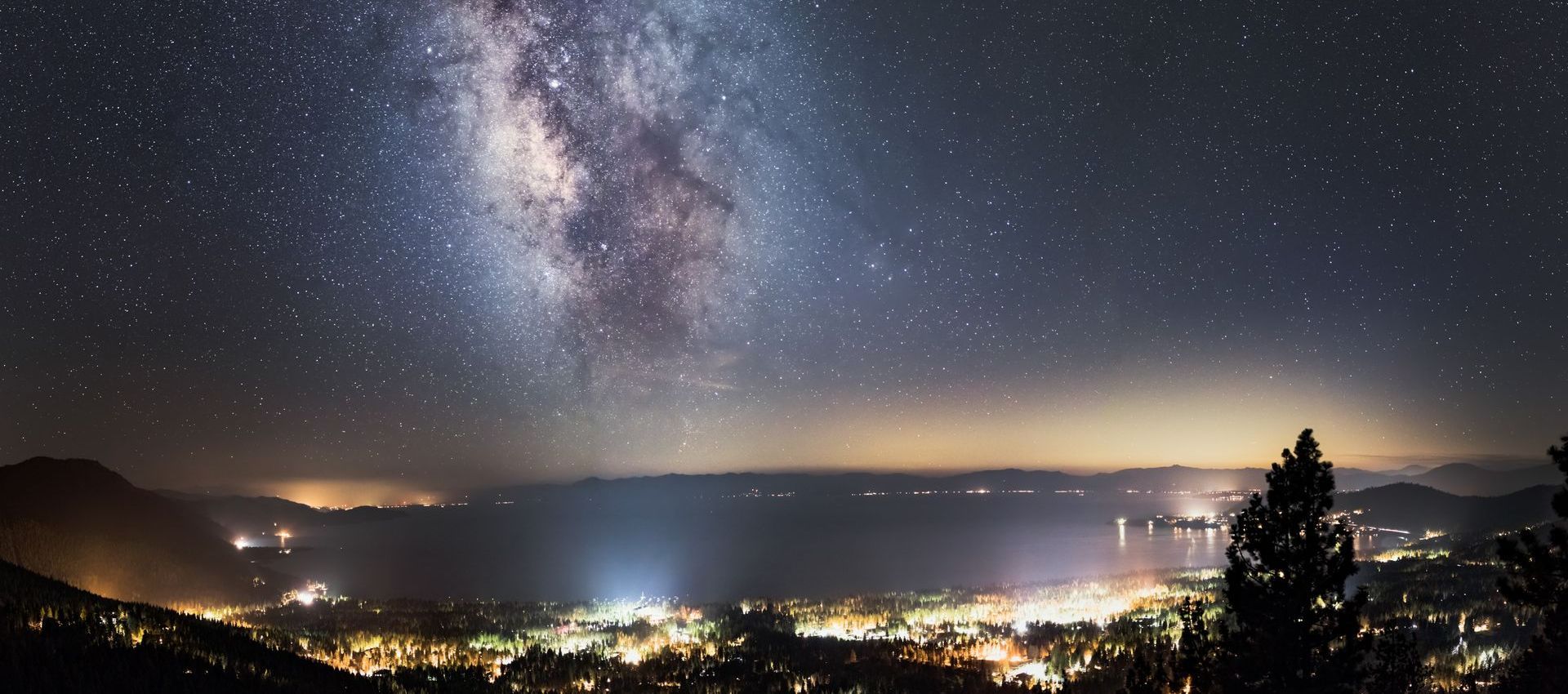 The milky way is visible over a city at night.