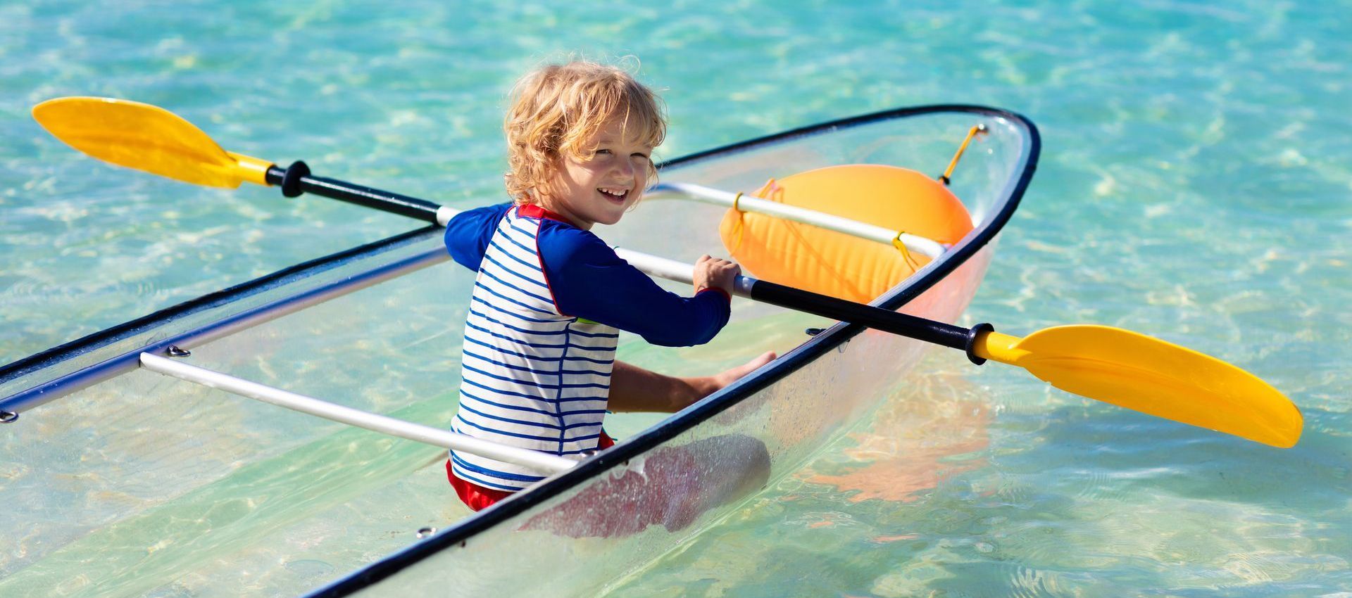 A young boy is paddling a clear kayak in the ocean.