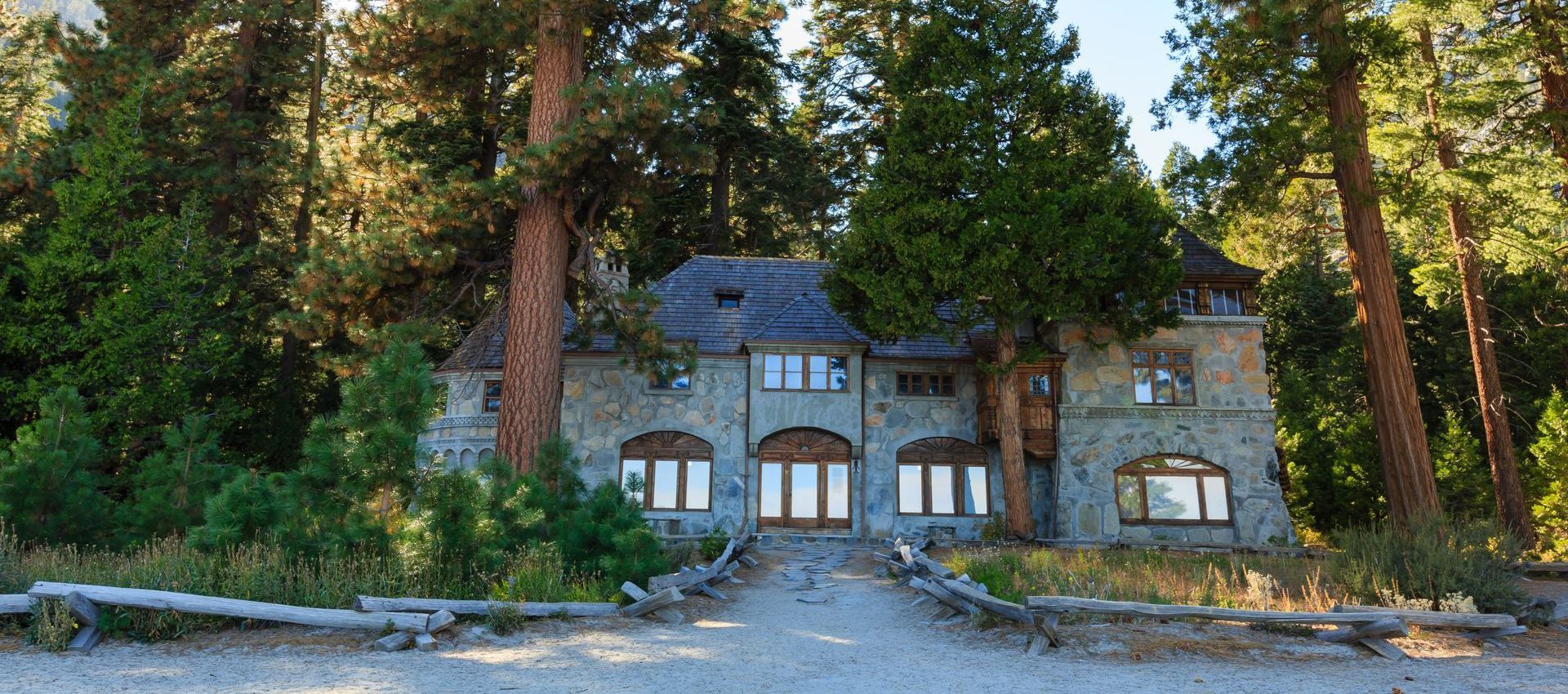 A large stone house is surrounded by trees in the middle of a forest.