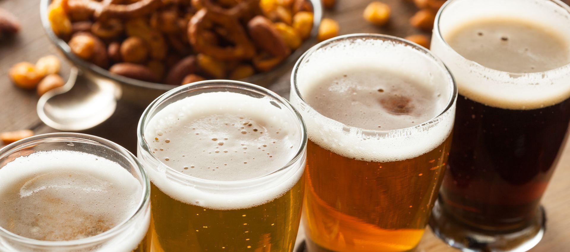 Four glasses of beer are sitting on a table next to a bowl of nuts.