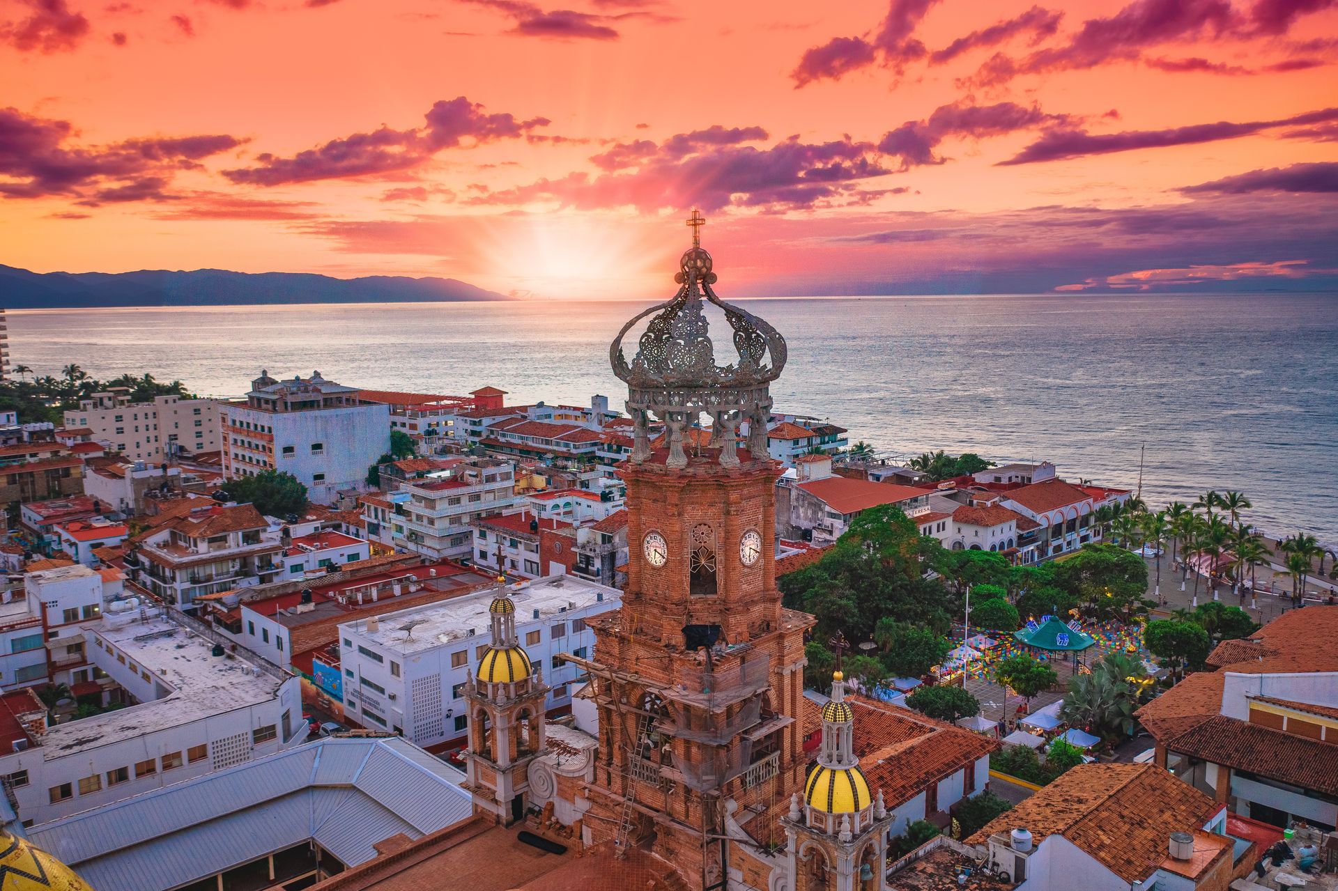 An aerial view of a city with a clock tower and a sunset over the ocean.