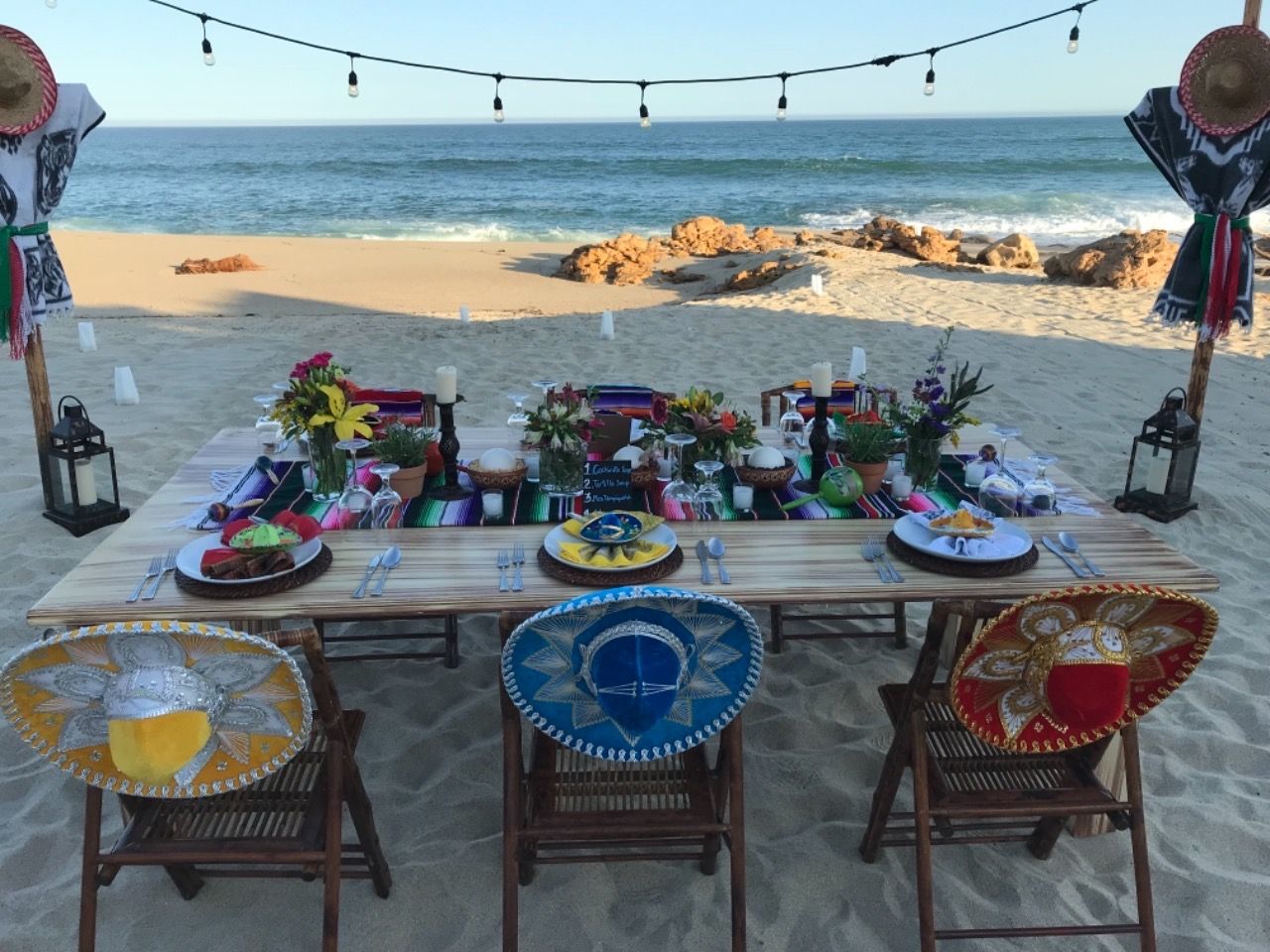 a table is set up on the beach with sombrero hats on the chairs