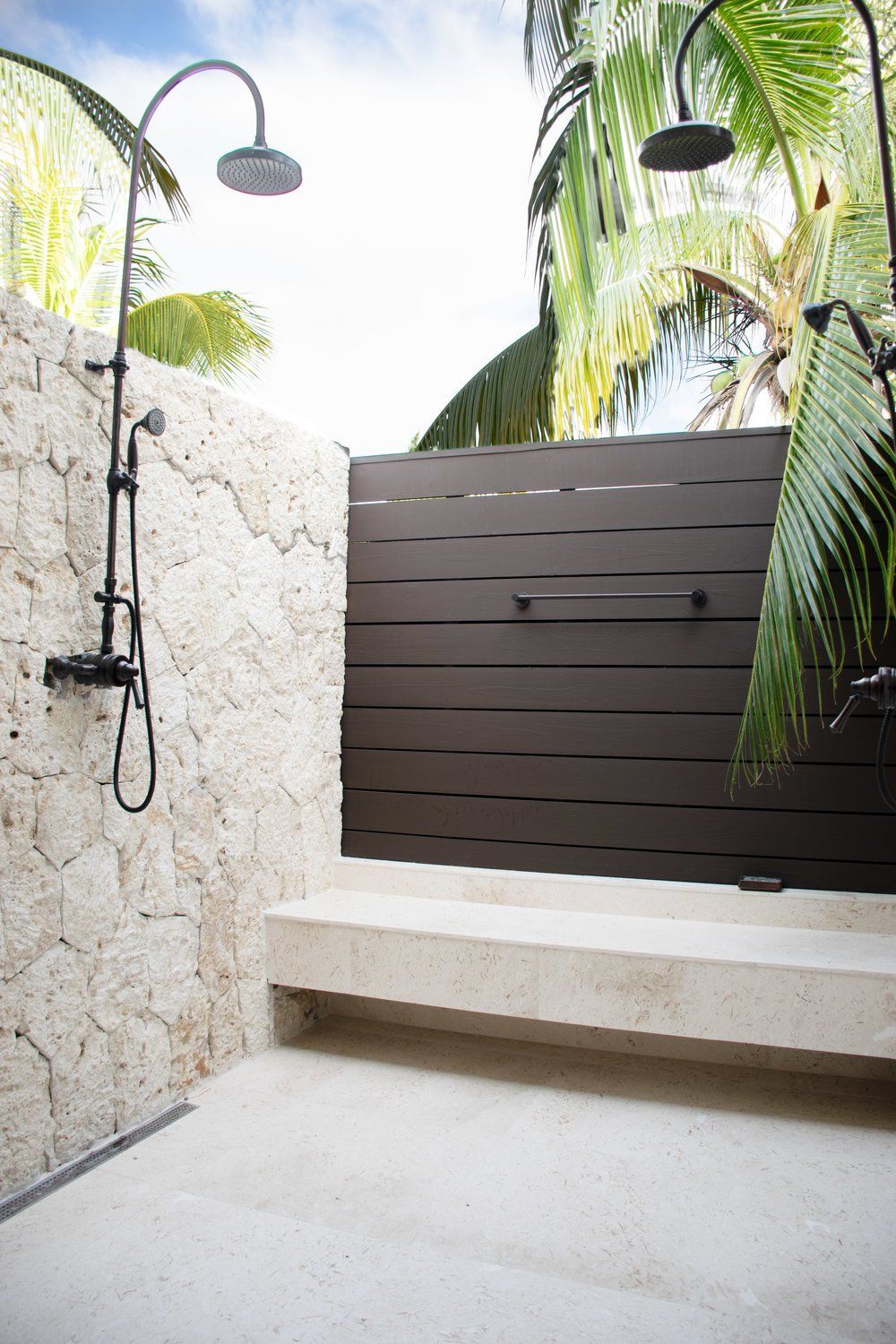 an outdoor shower with a bench and palm trees in the background