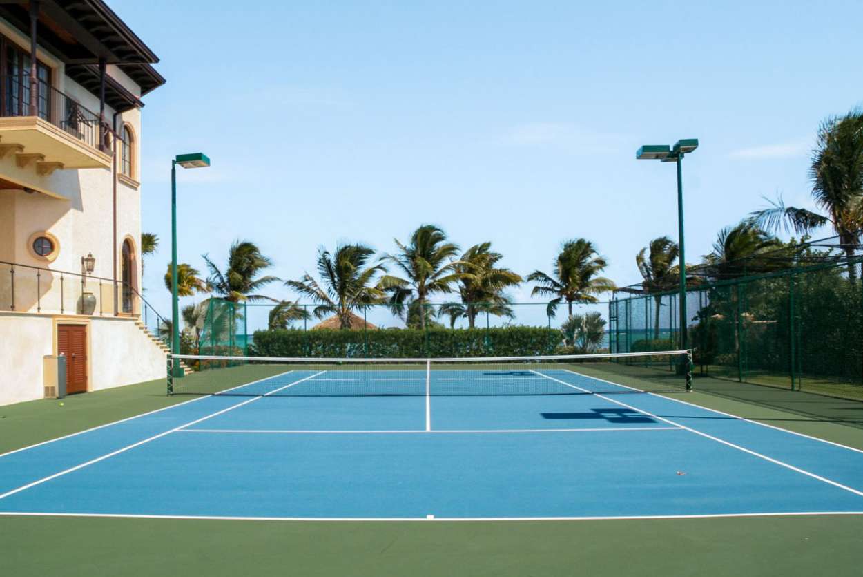 a tennis court in front of a house with palm trees in the background