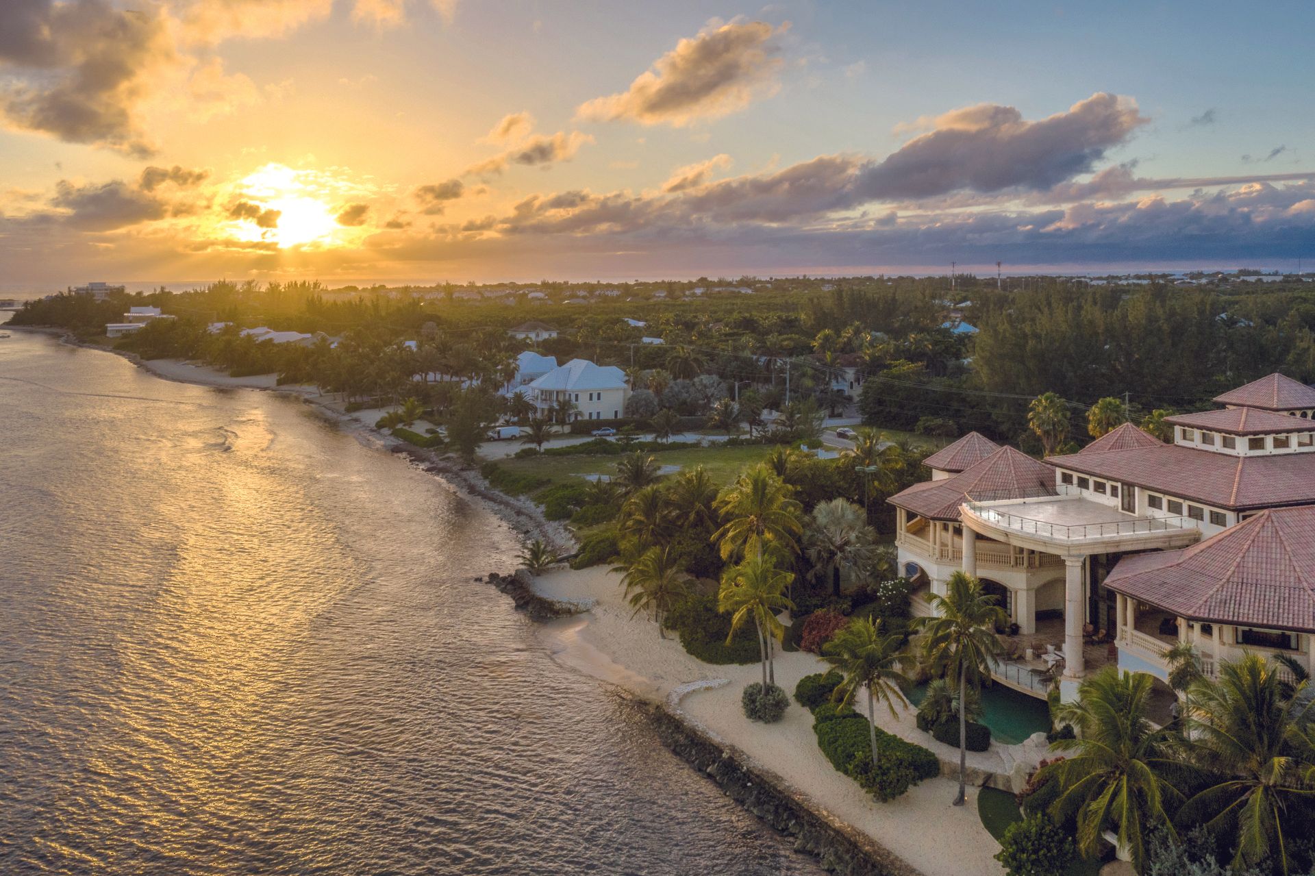 an aerial view of a large house next to a body of water at sunset