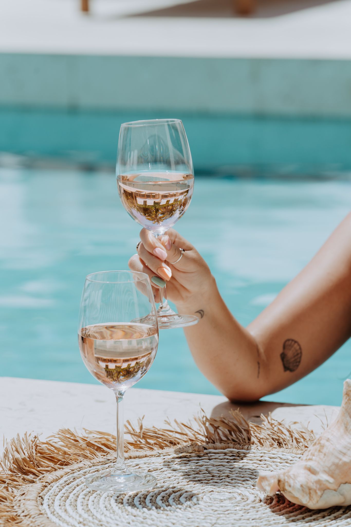 a woman is sitting by a pool holding two glasses of wine