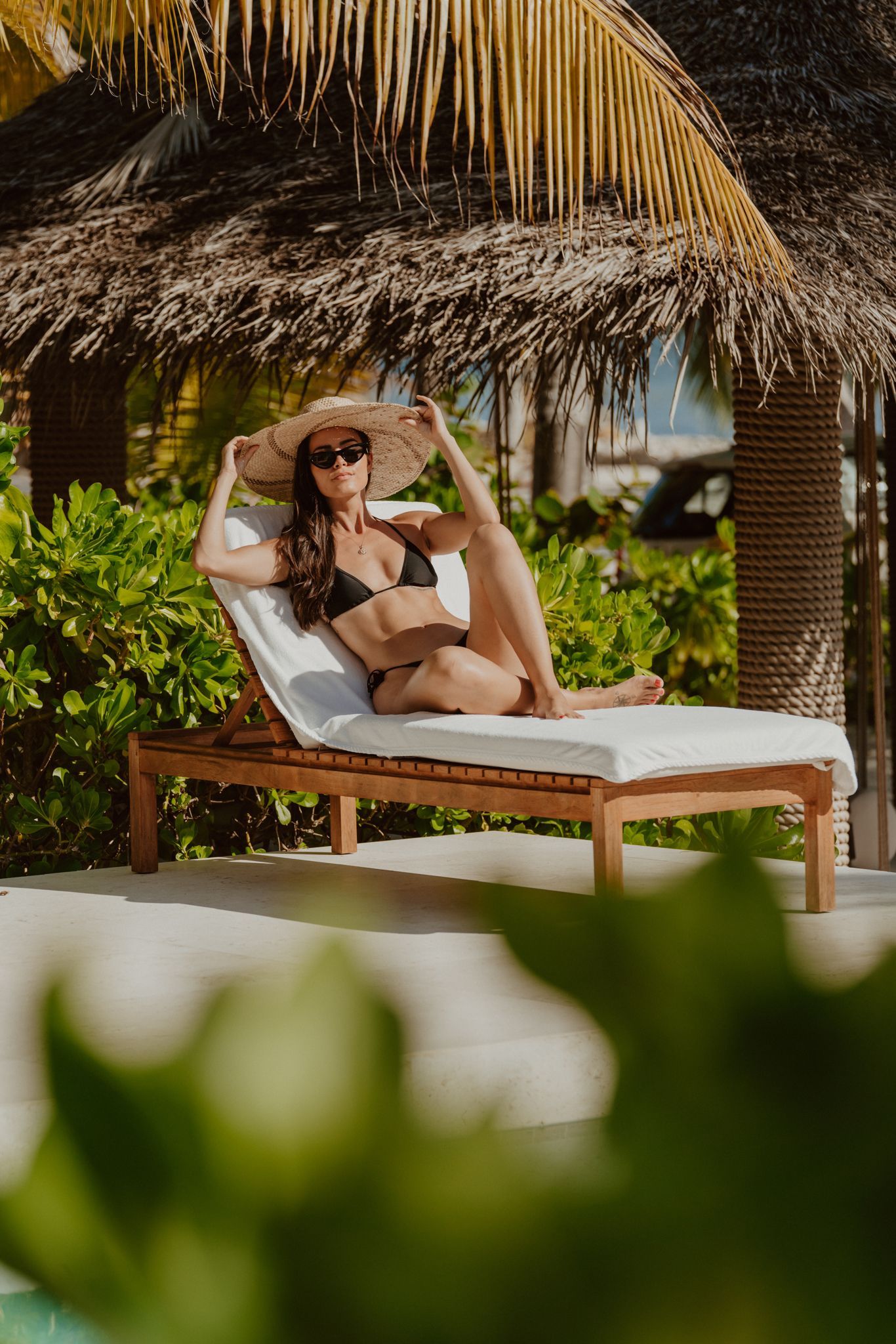 a woman in a bikini is sitting on a lounge chair under a palm tree