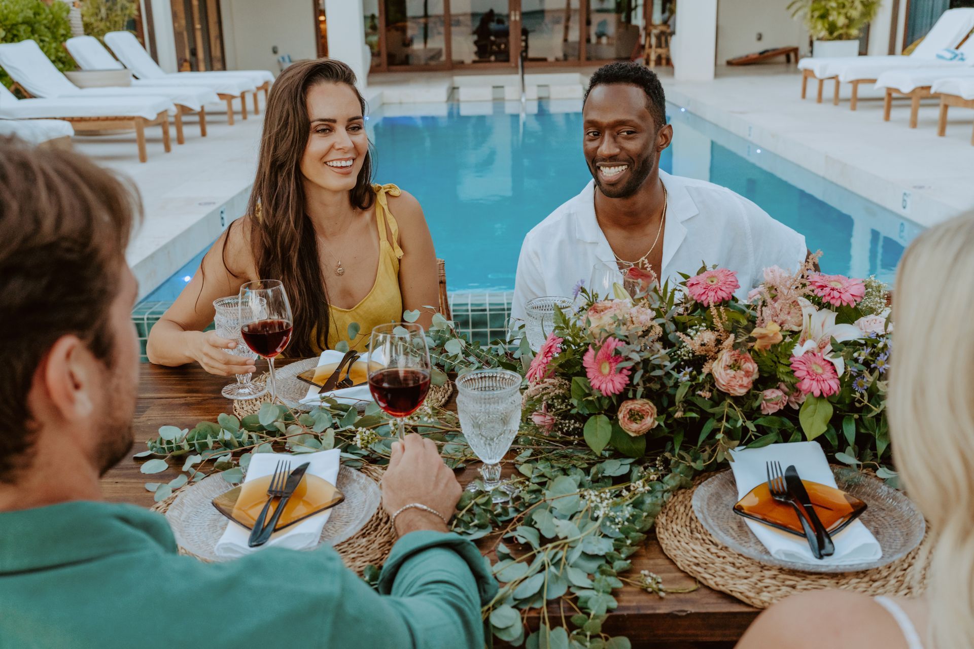 a group of people are sitting at a table in front of a swimming pool