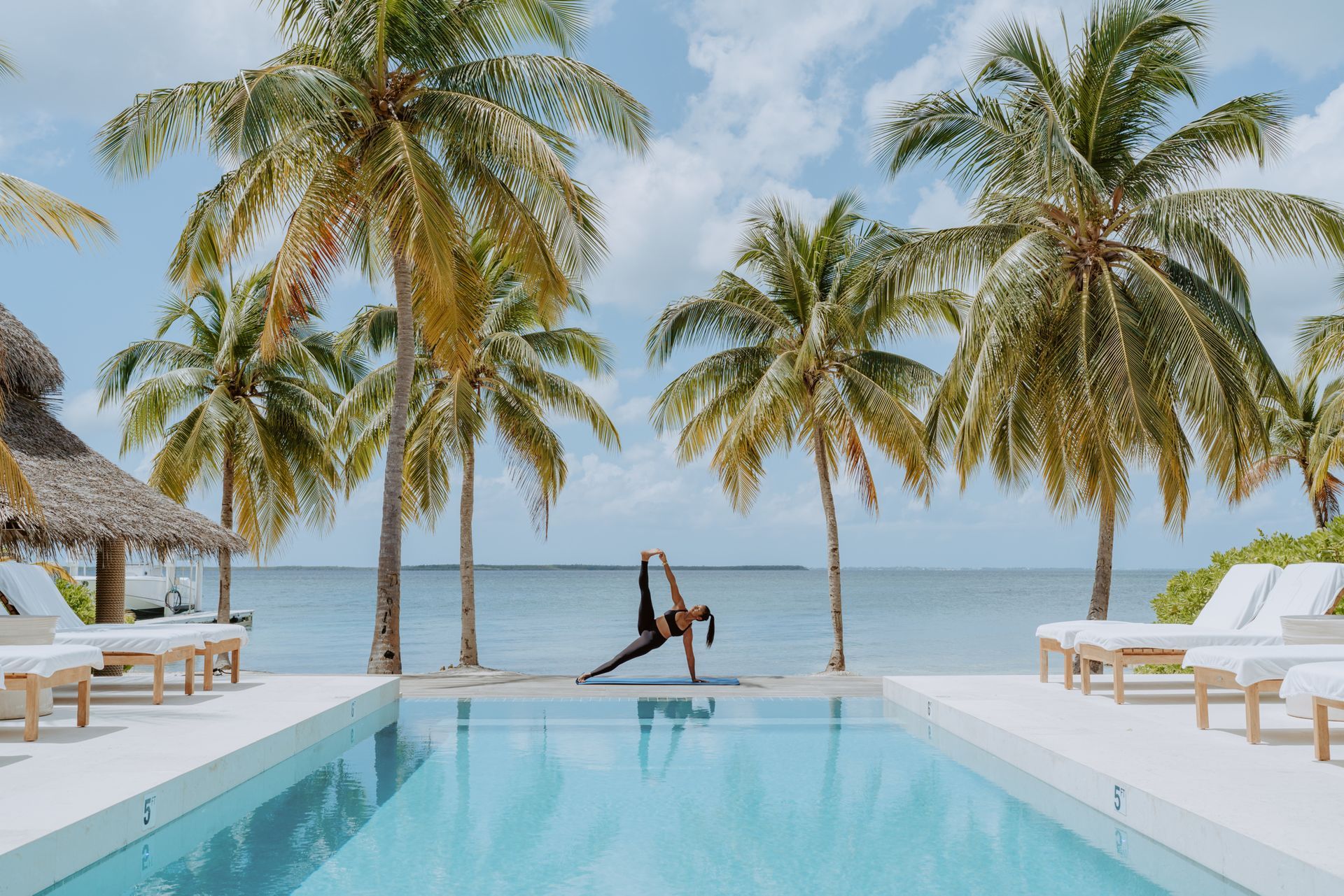 a woman is doing yoga in front of a swimming pool surrounded by palm trees