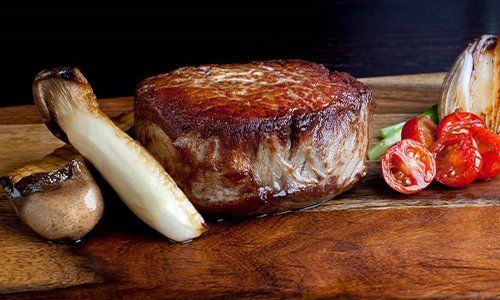a steak is sitting on top of a wooden cutting board next to mushrooms and tomatoes