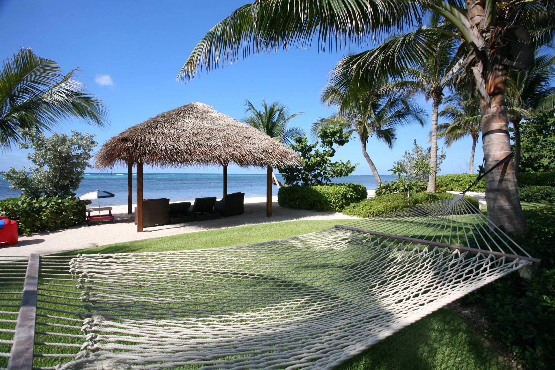 a hammock is sitting in front of a thatched hut on the beach