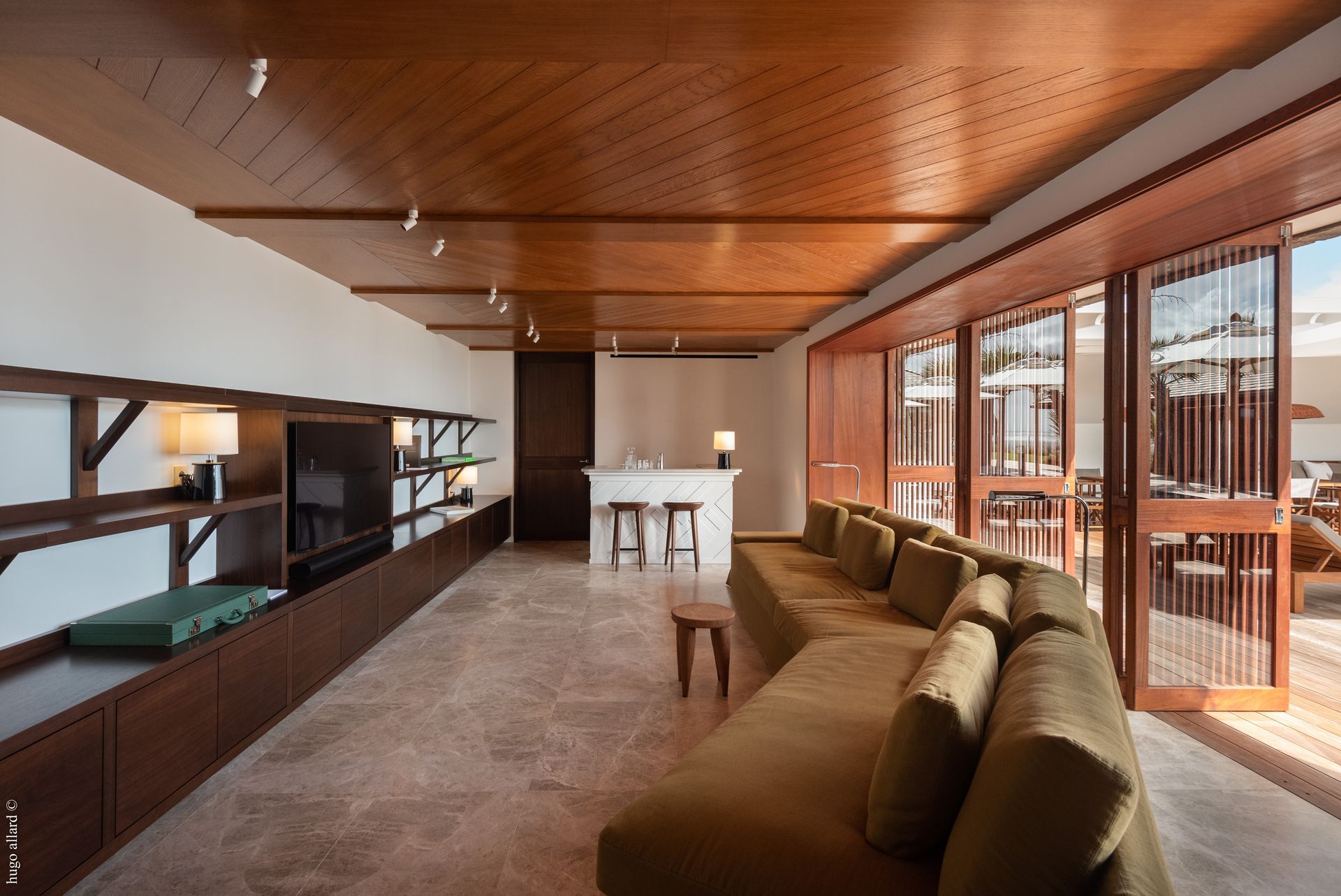 a living room with a couch, television, stools and a wooden ceiling