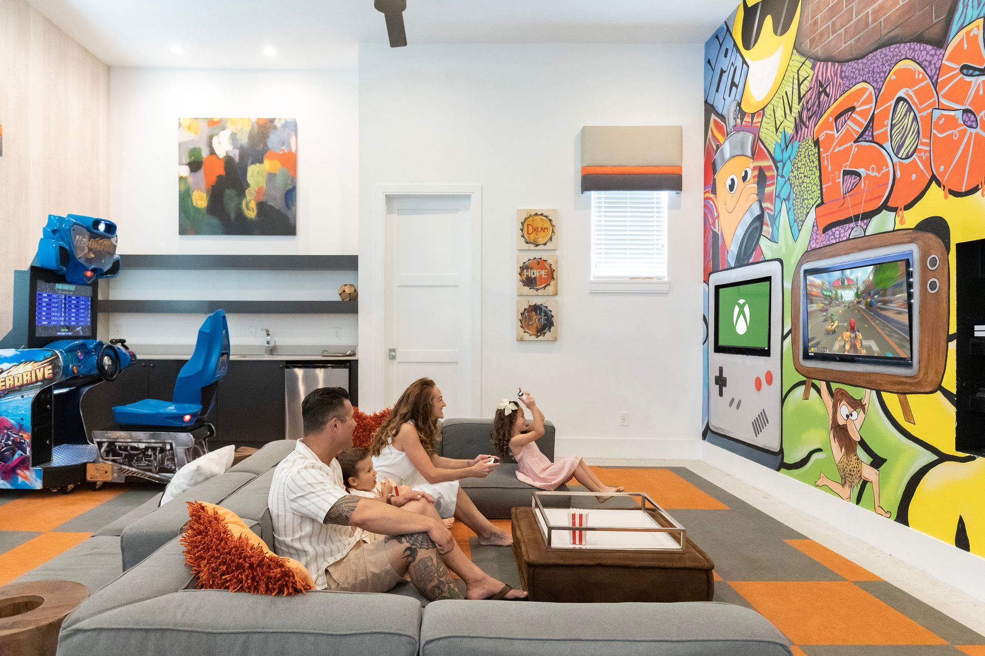 a family is sitting on a couch in a game room with a mural on the wall