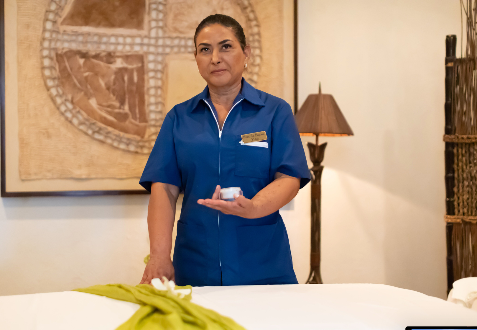 a woman in a blue uniform is standing in front of a massage table holding a container
