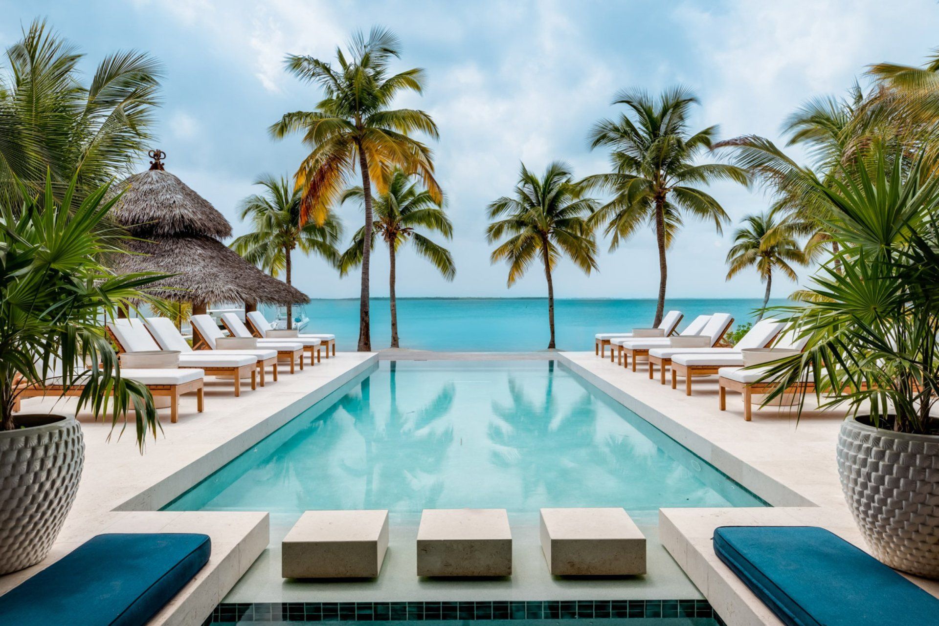 a large swimming pool surrounded by palm trees and chairs overlooking the ocean