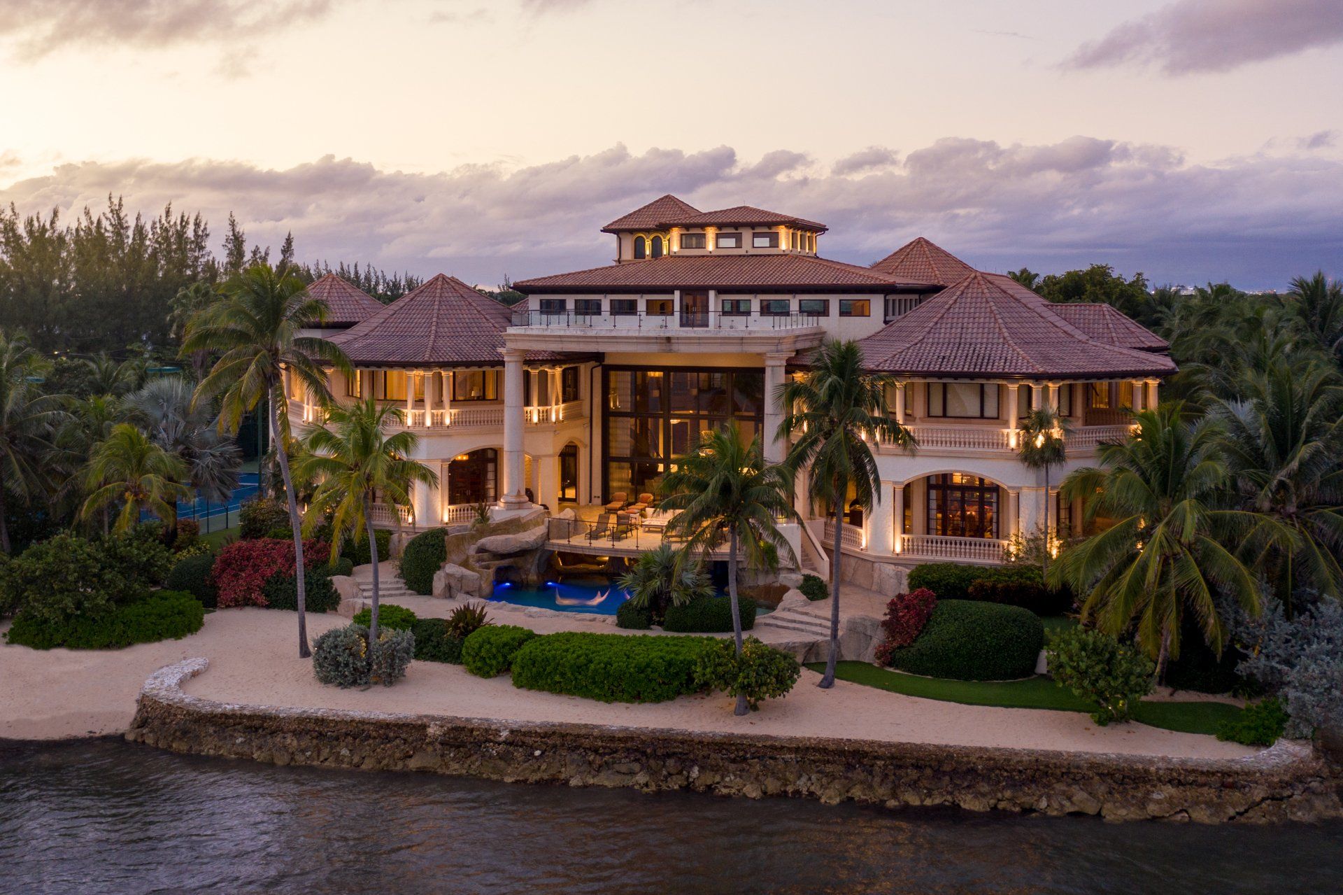 a large house is sitting on top of a lush green hill next to a body of water