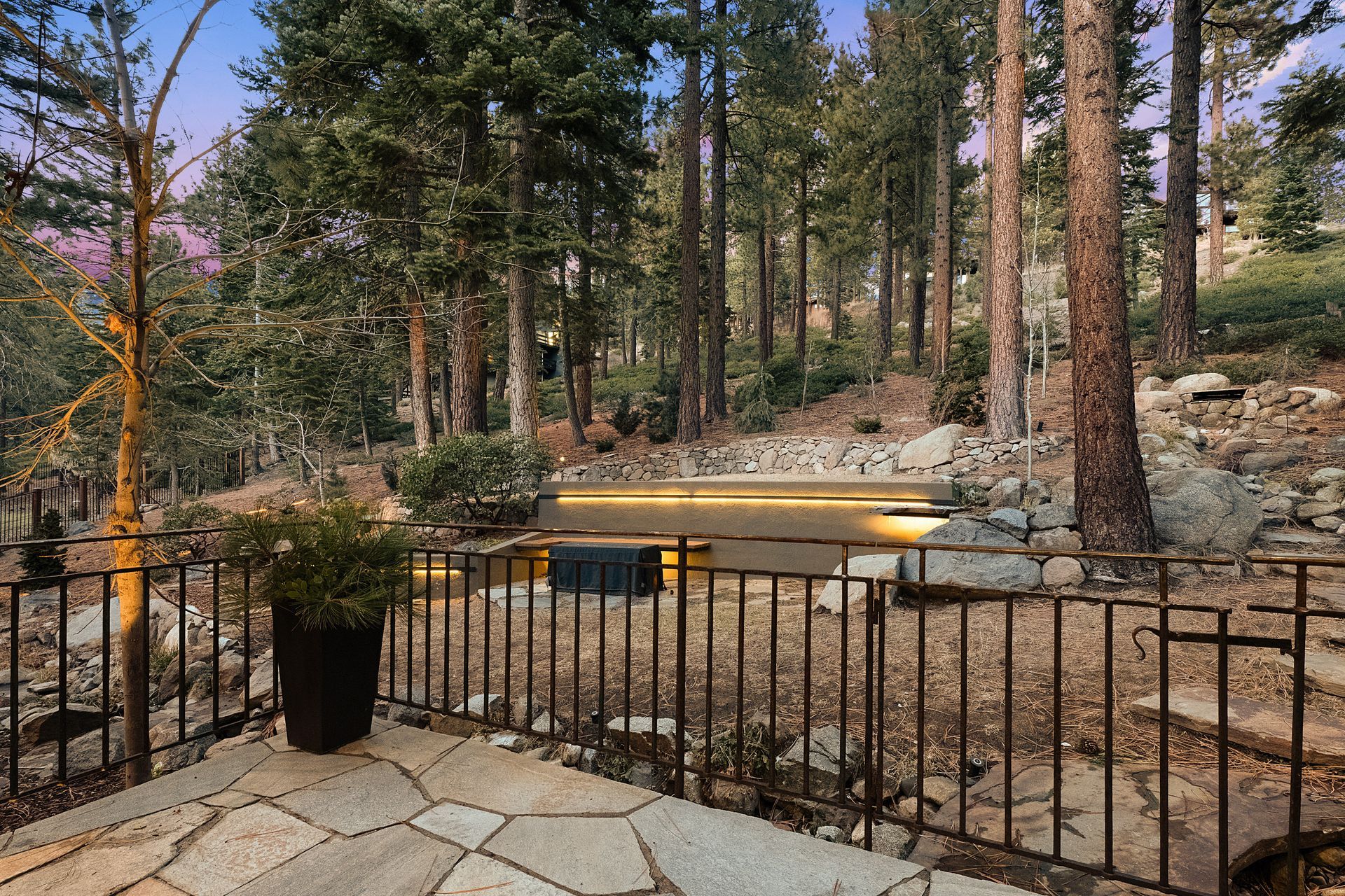 a patio with a fence and a pond in the middle of a forest