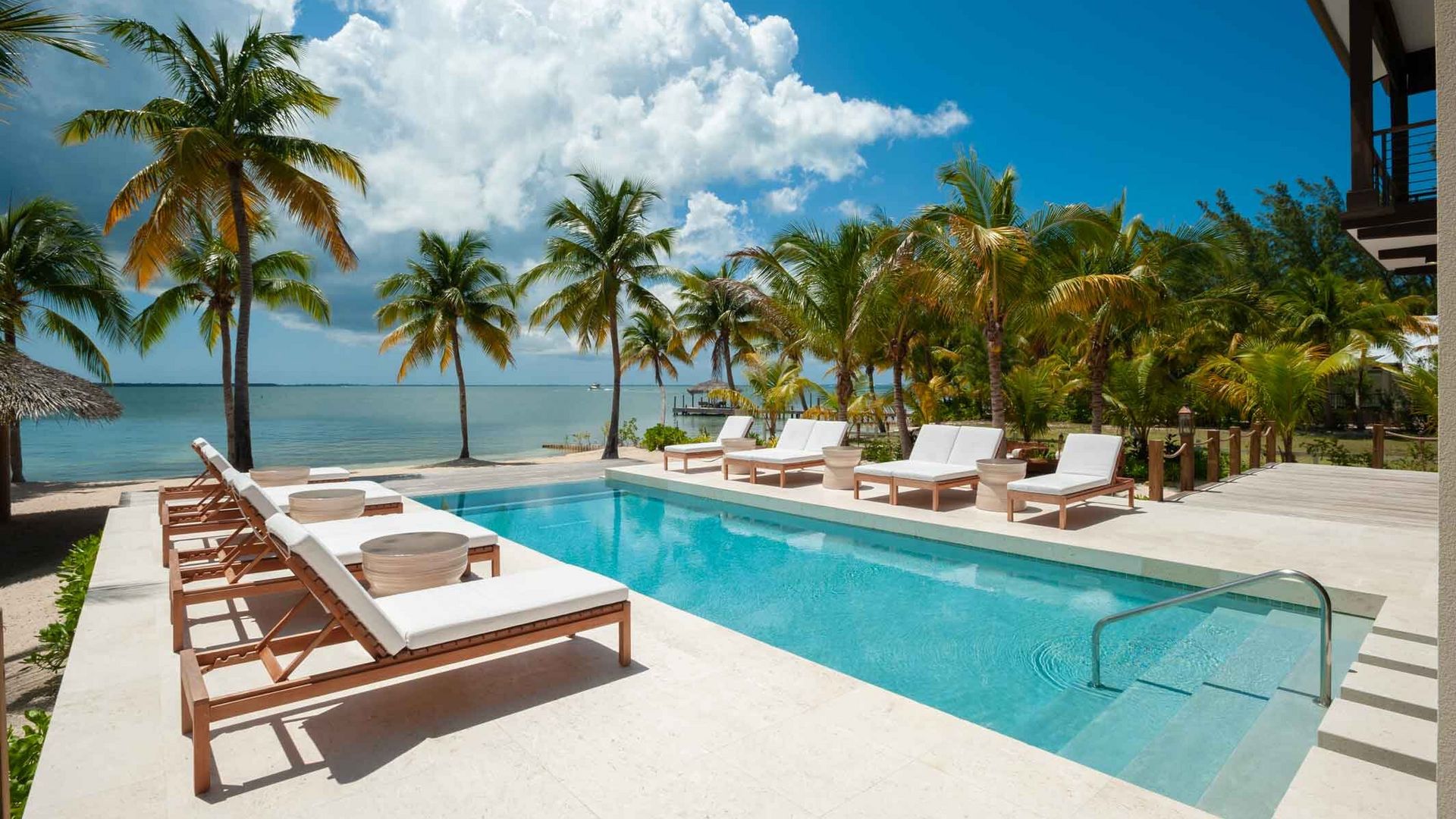 A large swimming pool surrounded by chairs and palm trees next to the ocean.