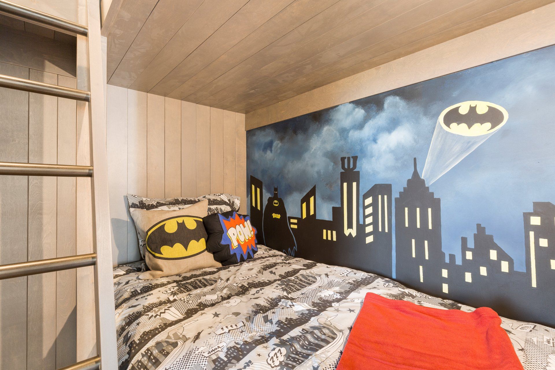 a bedroom with a bunk bed and a batman mural on the wall