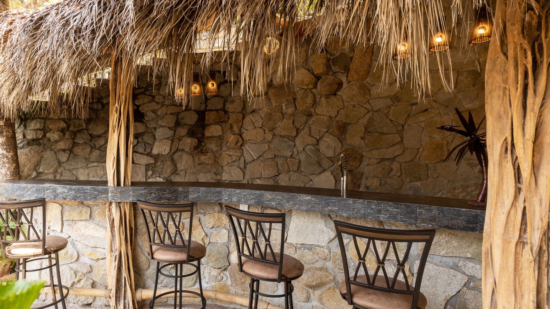 a thatched hut with a bar and chairs underneath it