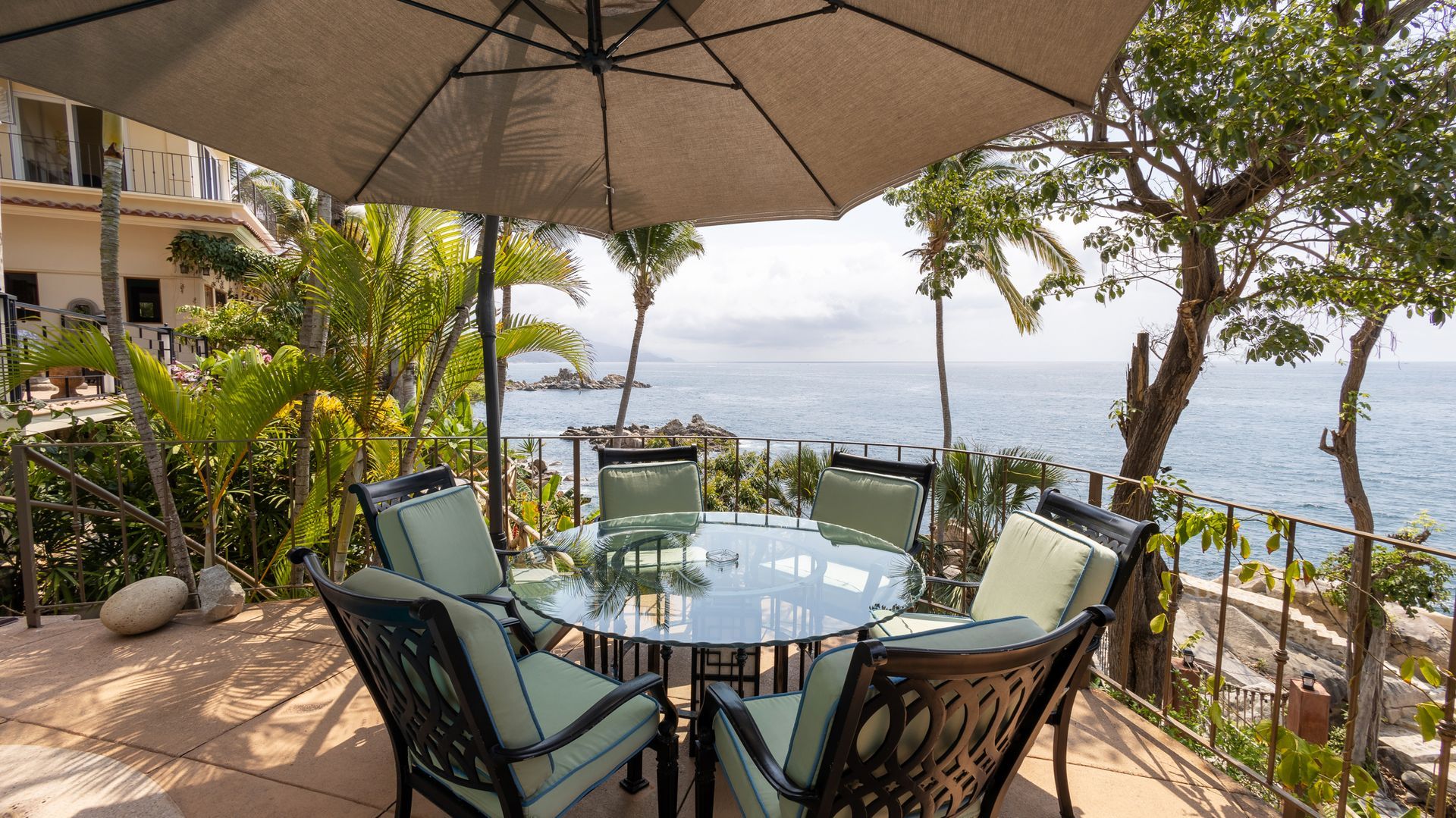 a patio with a table and chairs under an umbrella overlooking the ocean