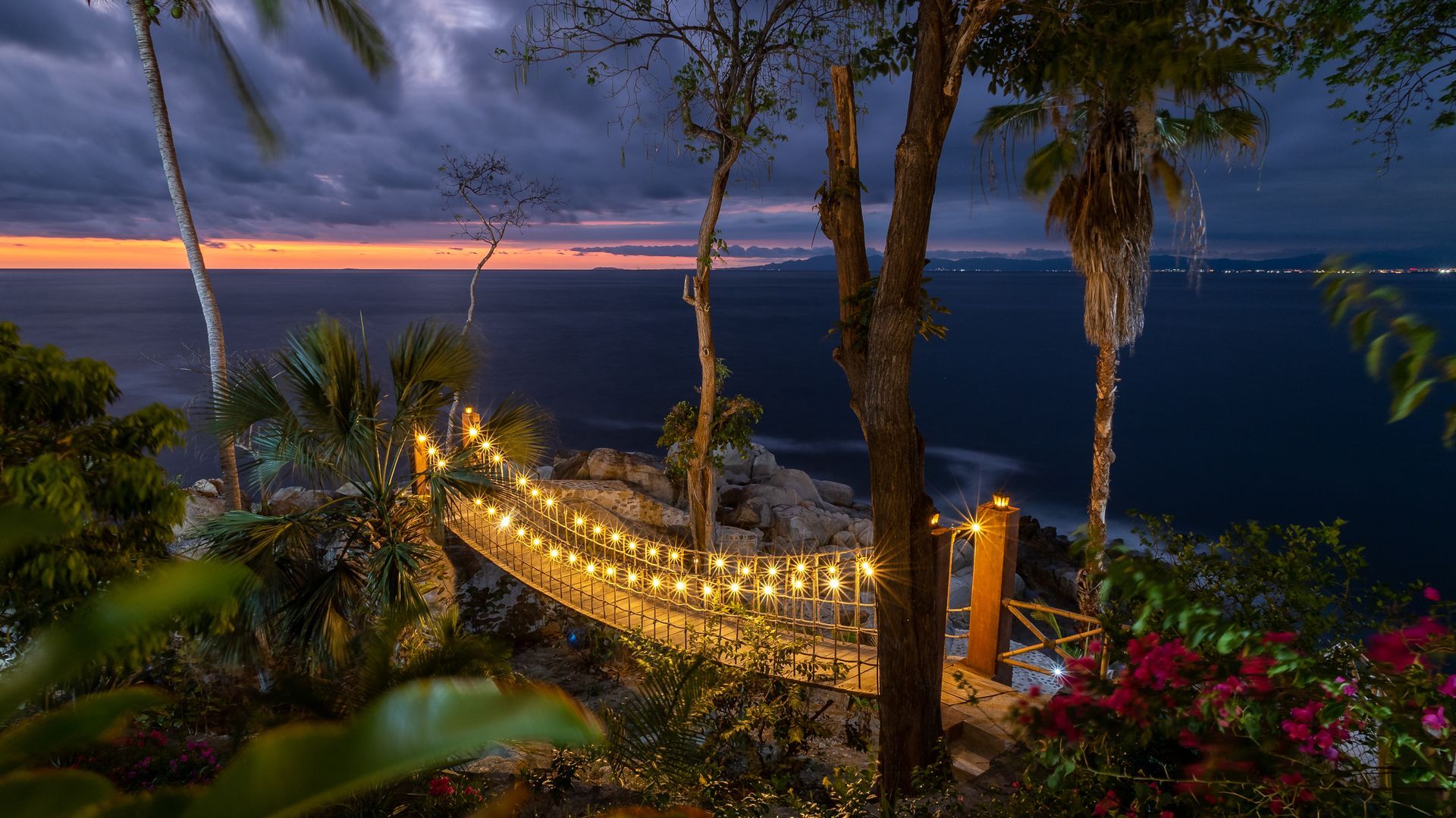 a hammock with lights hanging from trees overlooking the ocean at night