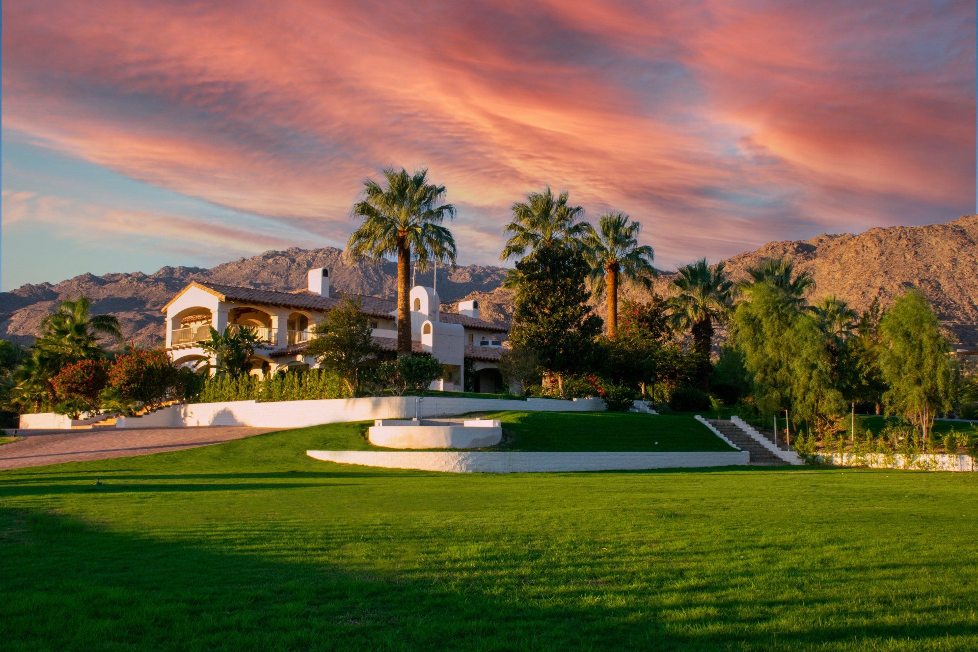 a large house is sitting on top of a lush green hill surrounded by palm trees