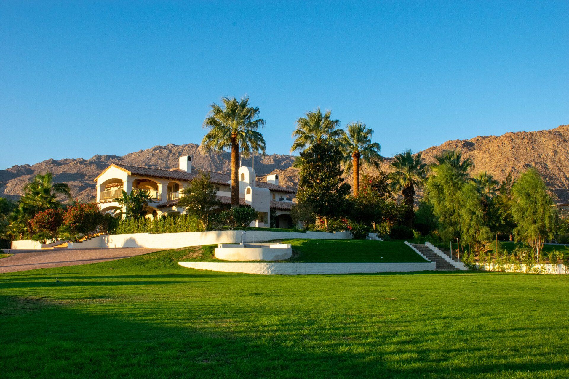 a large house with palm trees in front of it and mountains in the background