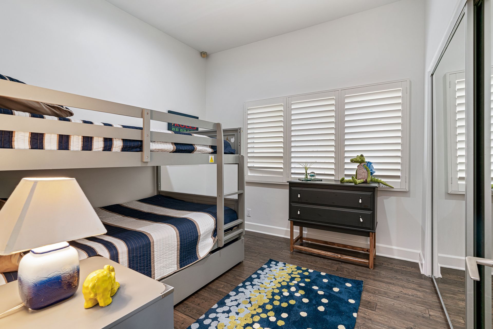 A bedroom with bunk beds , a dresser , a lamp , and a rug.